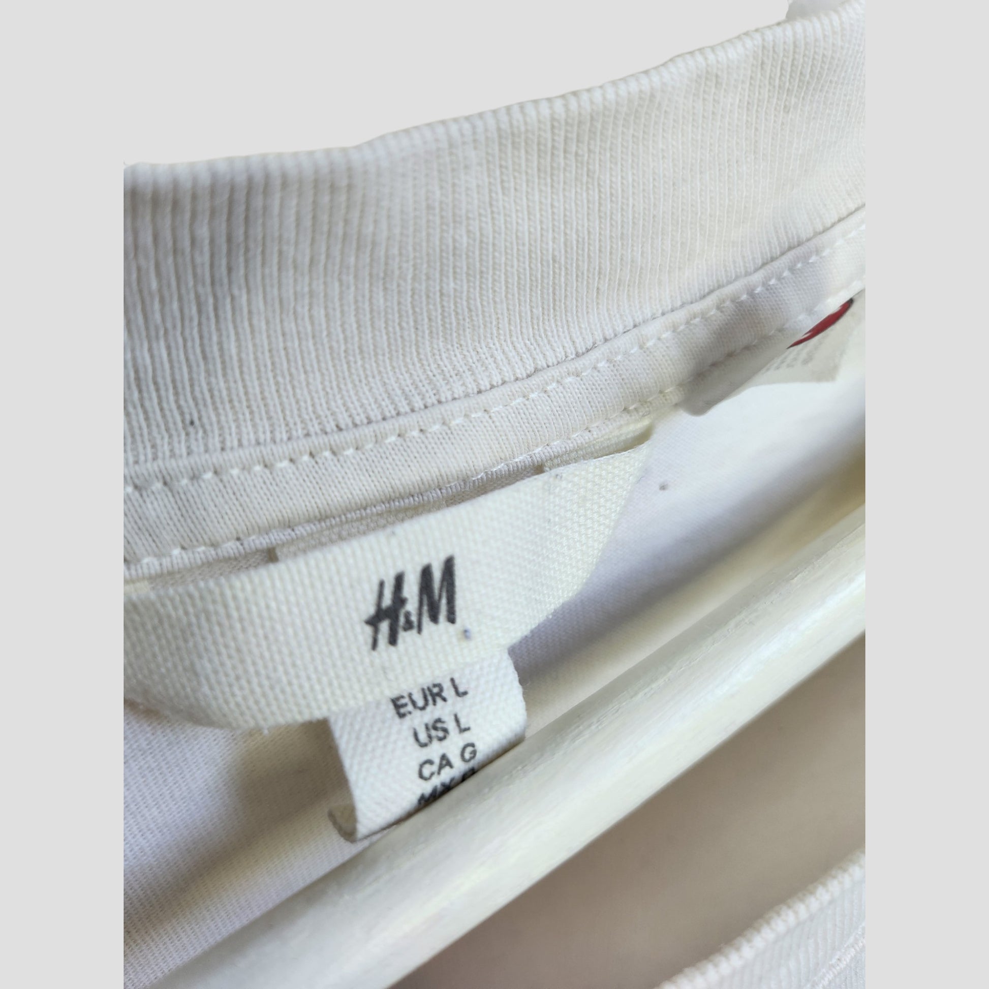 Close-up of a cream/red H&M Upcycled Breastfeeding & Pumping “The Rolling Stones” Band t-shirt (L, 100312) on a white hanger, showing the brand label—an example of eco-friendly preloved clothing.