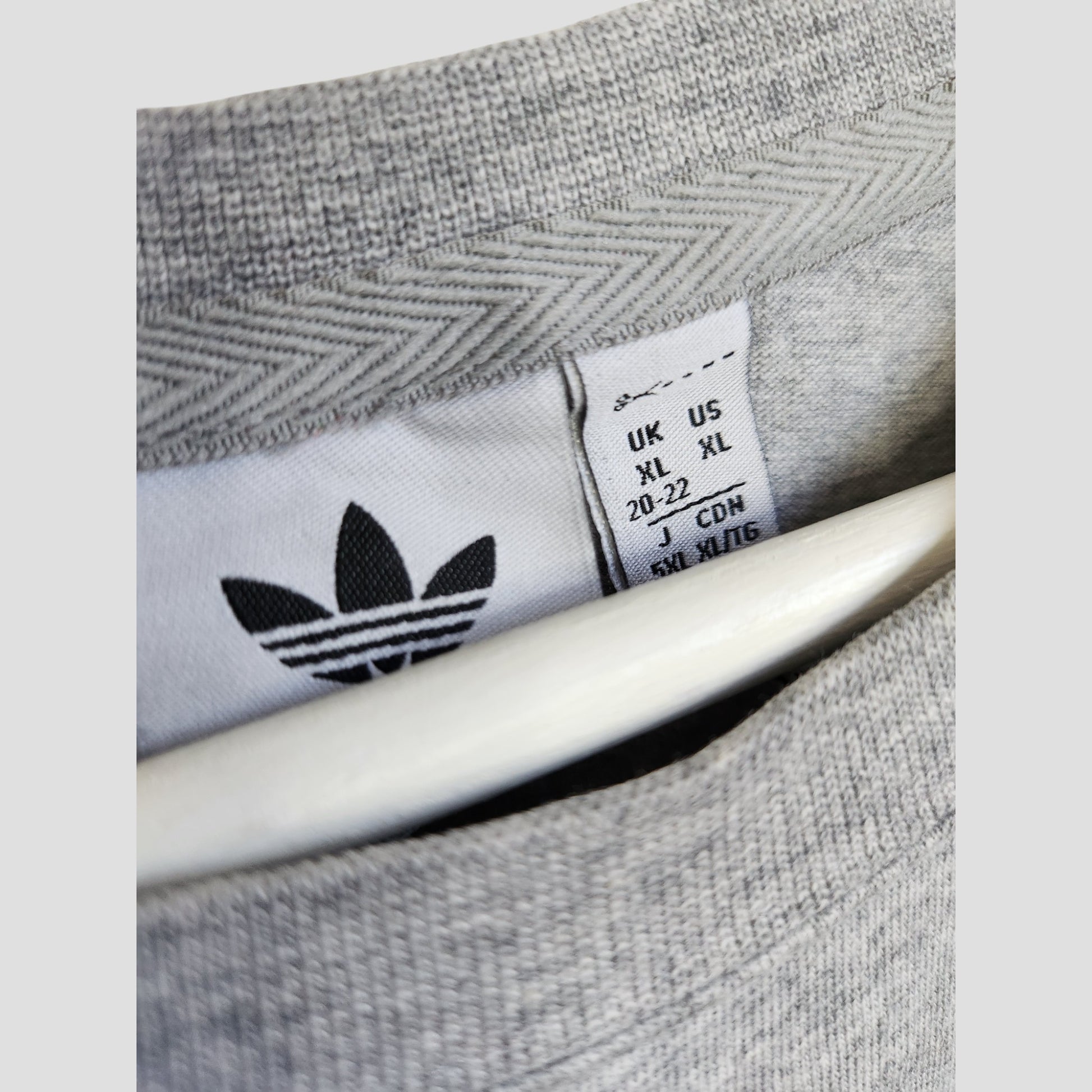 Close-up of an Adidas Originals Upcycled Breastfeeding & Pumping T-shirt (Grey/Green, XL UK20/22), showing the inside collar with sizes and the black trefoil logo. The eco-friendly piece is partially displayed on a white hanger.