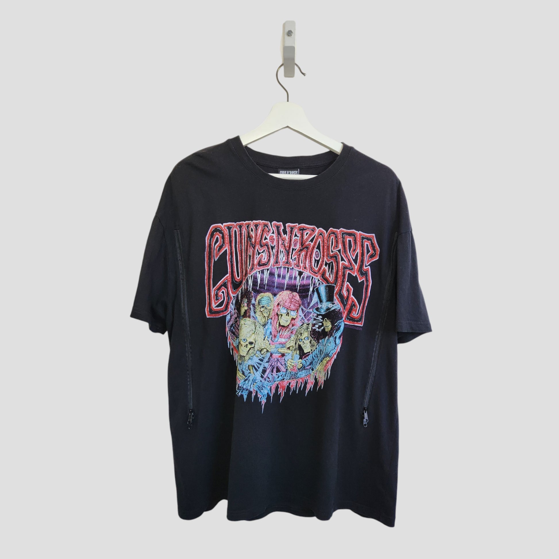 Primark Upcycled Breastfeeding & Pumping Black Guns N' Roses Band t-shirt (L, UK14/16) features colorful logos and skulls on the front. Crafted from upcycled nursing wear, it's an eco-friendly choice. Displayed on a hanger against a light gray background.
