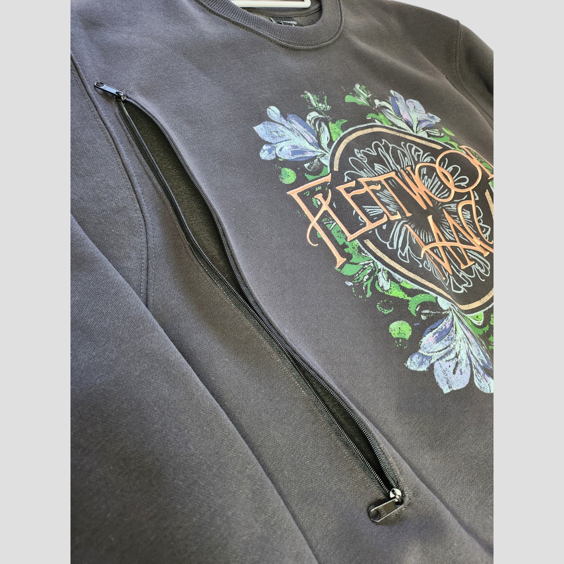 A close-up of Primark’s upcycled oversized Fleetwood Mac band sweatshirt (L), featuring embroidered graphics and a diagonal side zipper—crafted from preloved clothing for an eco-friendly, affordable breastfeeding & pumping option.