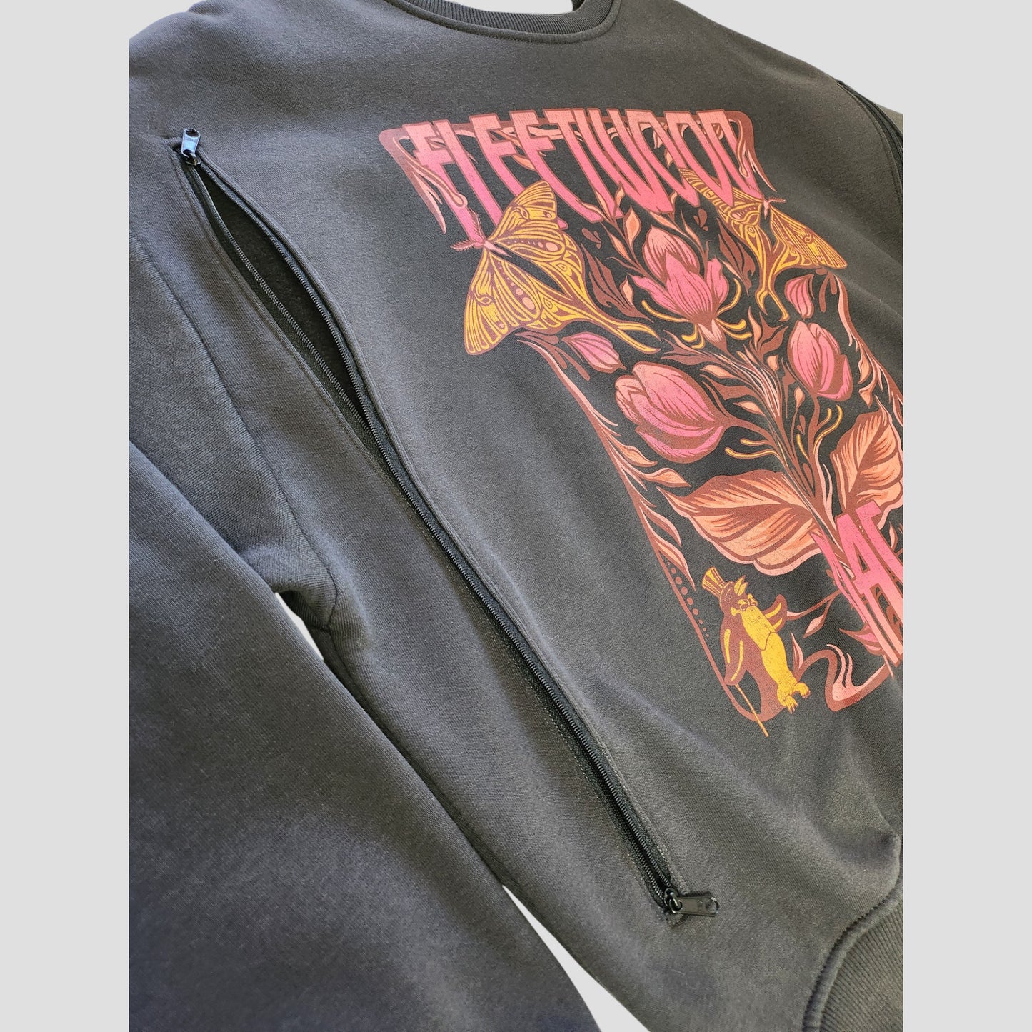 Primark’s upcycled dark grey Fleetwood Mac floral band oversized sweatshirt (M) features nursing-friendly diagonal zippers, flowers, moths, and a small yellow animal—an eco-friendly choice for breastfeeding and pumping.