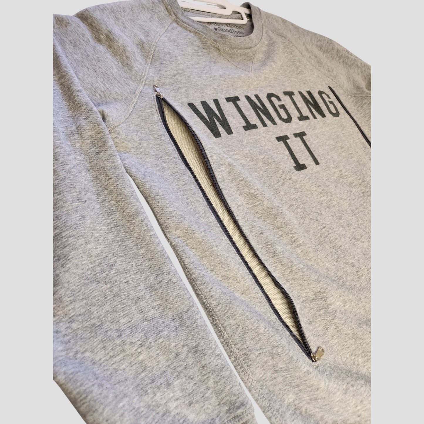 The Selfish Mother Upcycled Breastfeeding & Pumping Grey WINGING IT Sweatshirt M (100199) features bold black text and diagonal zippers for discreet nursing—making it a stylish, eco-friendly choice for moms.