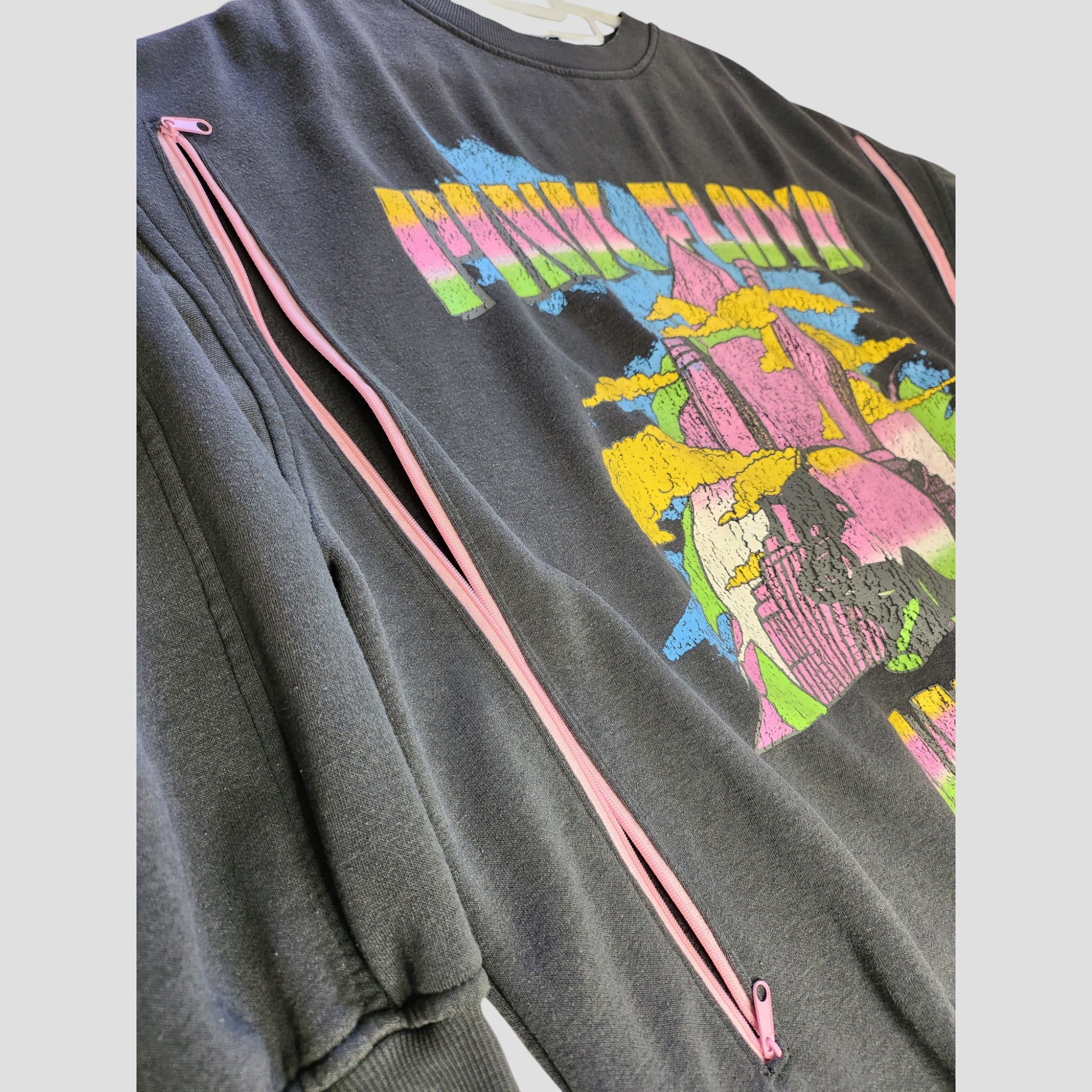 Displayed on a hanger against a neutral background, the H&M Upcycled Breastfeeding & Pumping Pink Floyd Band Oversized Sweatshirt (L, 100176) features pink sleeve zippers and a colorful abstract graphic.