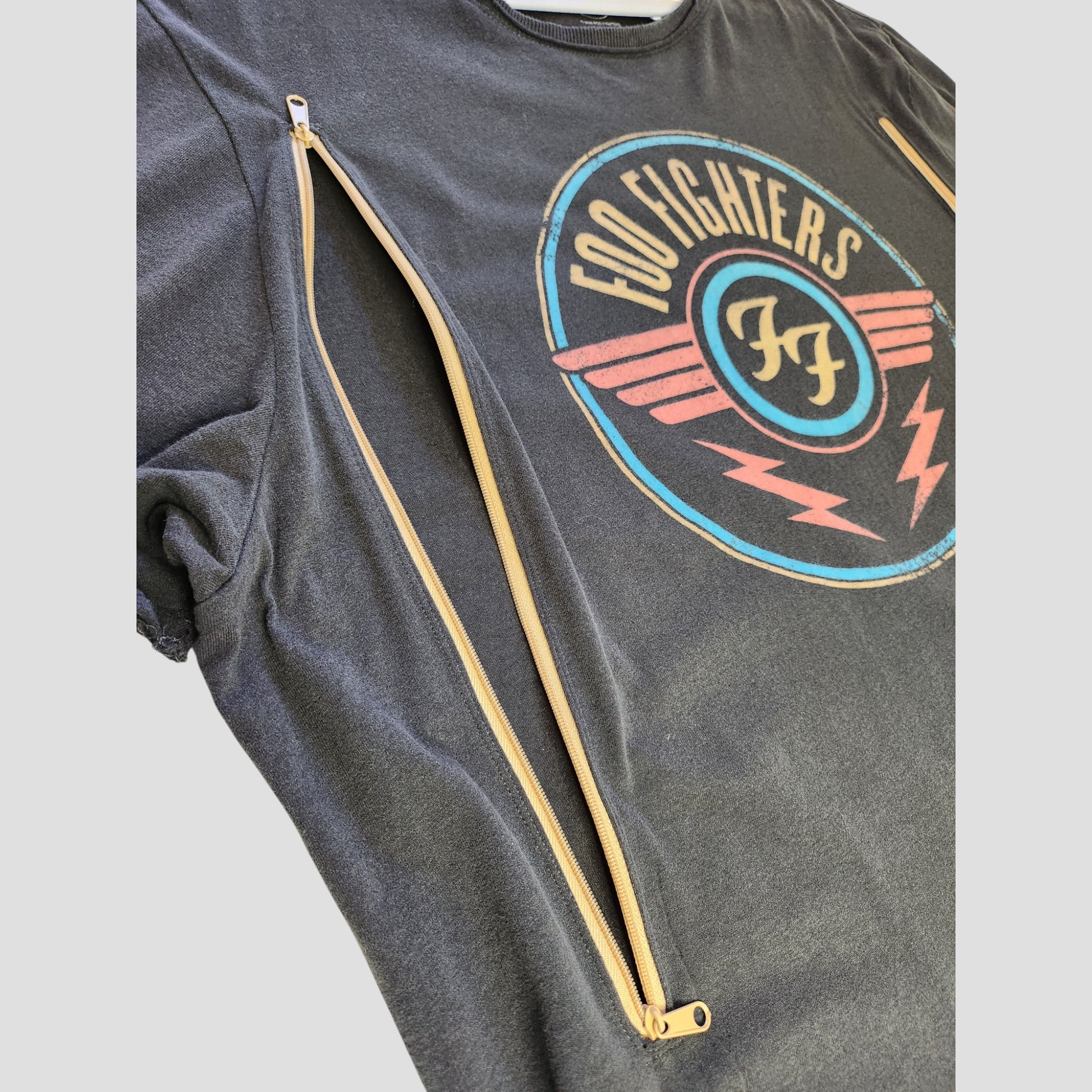 The Amplified Upcycled Breastfeeding & Pumping Grey Foo Fighters Band t-shirt 3XL (100329) features a round logo and two long diagonal tan zippers—an eco-friendly choice for music-loving nursing moms.