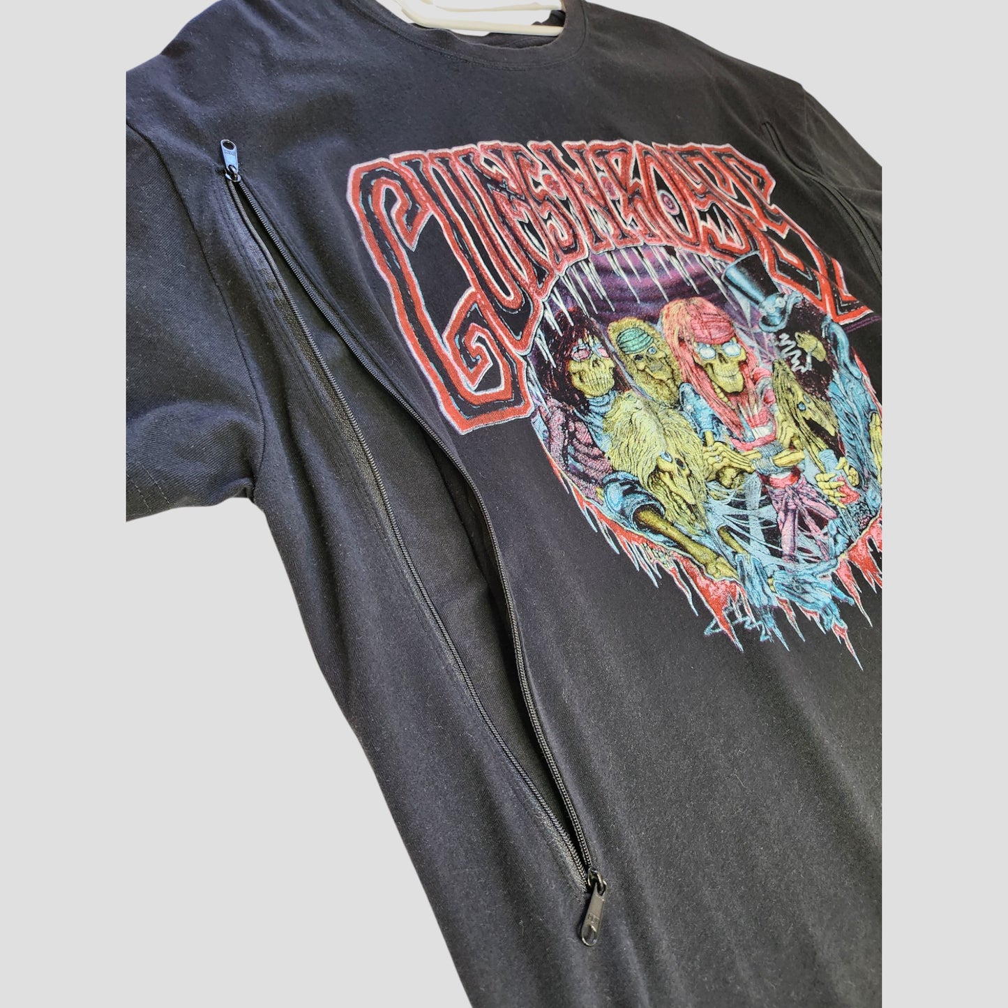 Close-up of a Primark Upcycled Breastfeeding & Pumping Black Guns n' Roses Band t-shirt (L, UK14/16), featuring band illustrations and a diagonal shoulder-to-hem zipper for nursing convenience.