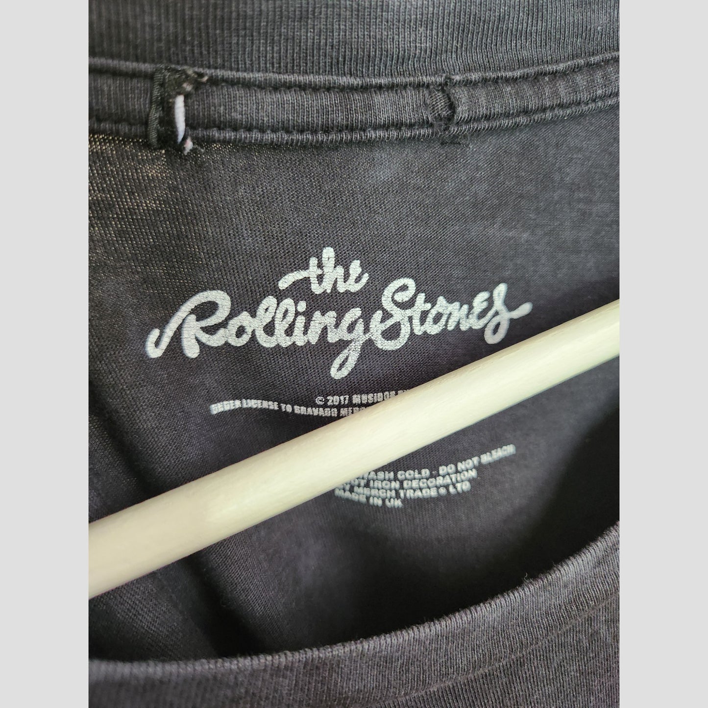 Close-up of a Boohoo Upcycled Breastfeeding & Pumping Black The Rolling Stones Band t-shirt dress (UK8) collar with logo and care instructions in white, printed inside the neck. Displayed on a wooden hanger, this eco-friendly dress is perfect for sustainable style fans.