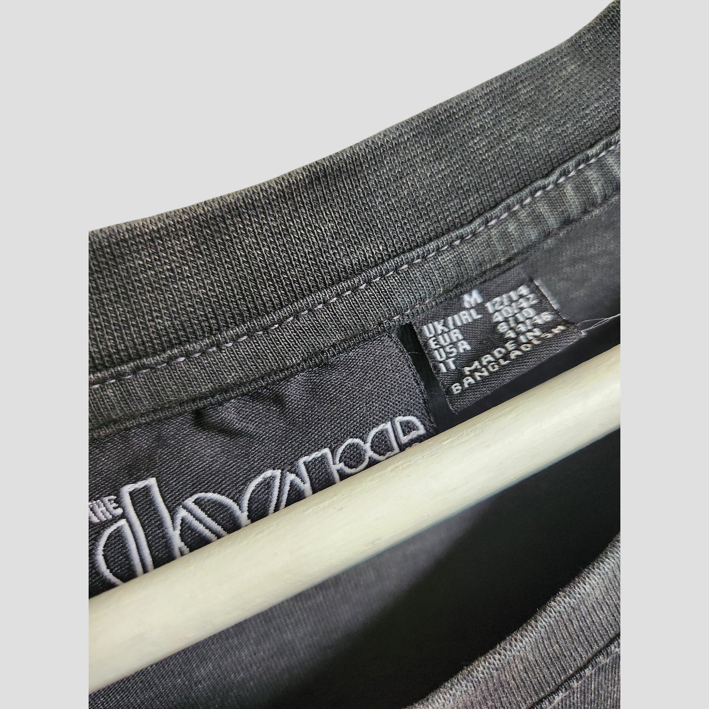 Close-up of a Primark black t-shirt dress collar with size info (UK, USA, EU) and “Made in Bangladesh” on the tag. Features a partial white logo—perfect for those after affordable, upcycled maternity or eco-friendly nursing wear.