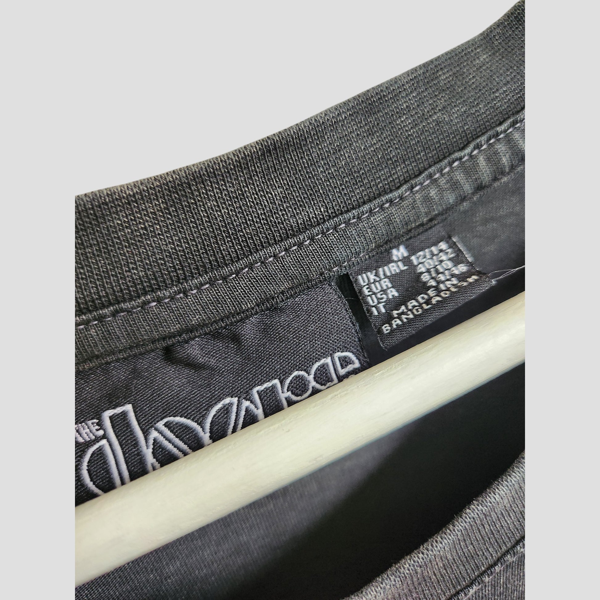 Close-up of a Primark black t-shirt dress collar with size info (UK, USA, EU) and “Made in Bangladesh” on the tag. Features a partial white logo—perfect for those after affordable, upcycled maternity or eco-friendly nursing wear.