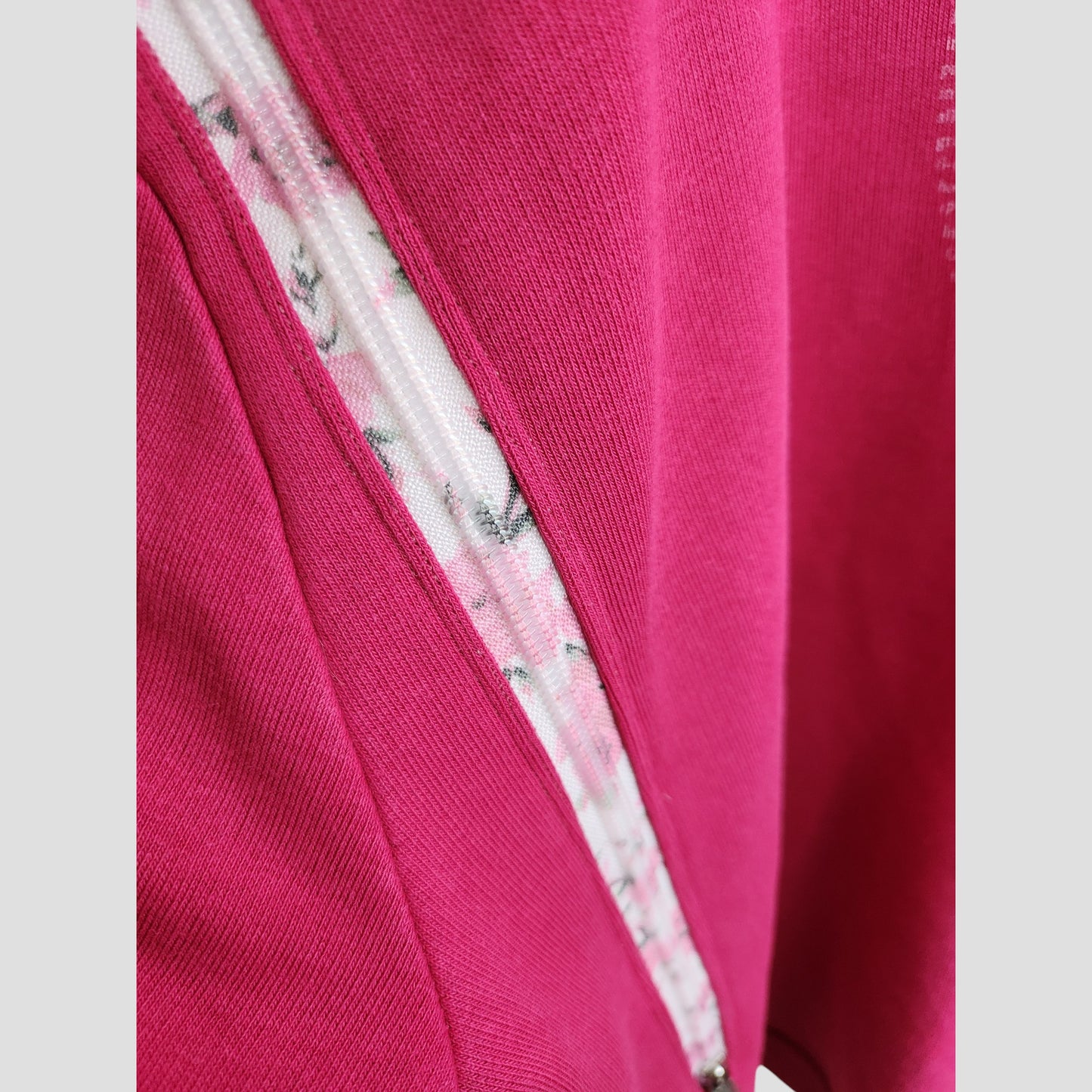 Close-up of the Human Milk Upcycled Breastfeeding & Pumping Hoodie (L, 100216) with a partially unzipped zipper, revealing a white inner fabric with a pink and gray floral pattern—eco-friendly maternity fashion.