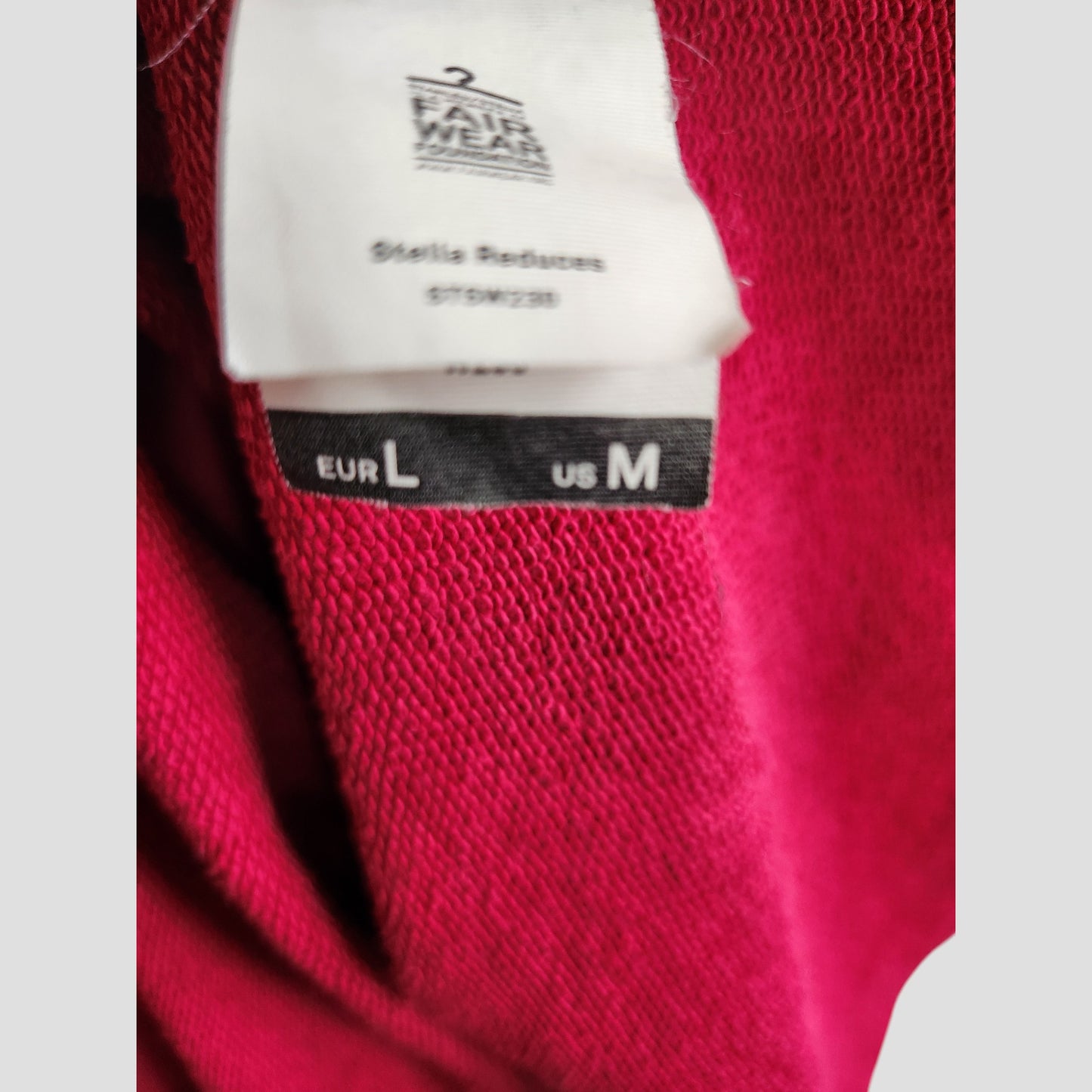 A close-up shows a Human Milk hoodie label on a red garment: European size L, US size M. The upper label hints at upcycled breastfeeding and pumping wear with care instructions from the Human Milk brand.