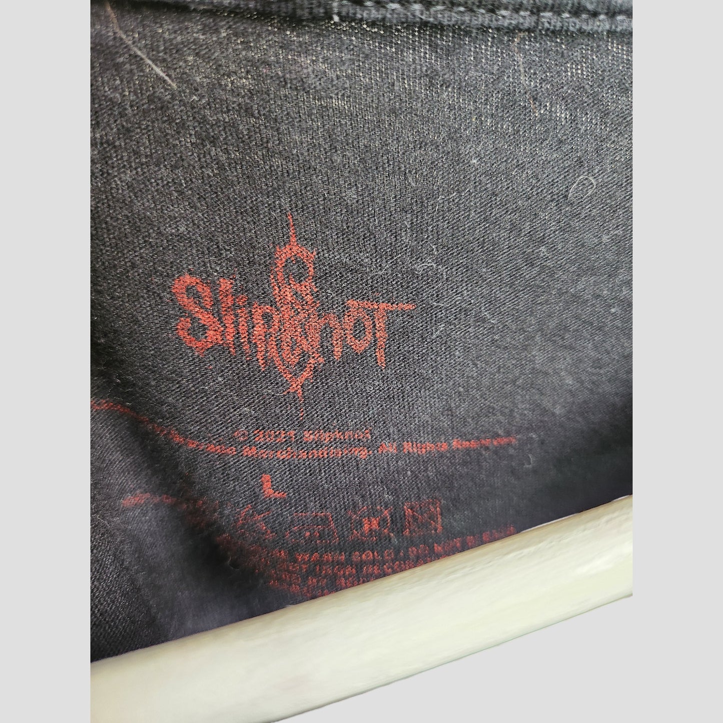 Close-up of the inside label area on an upcycled Slipknot breastfeeding & pumping t-shirt (size L), showing black fabric with red graphics, the Slipknot logo, and printed care instructions.