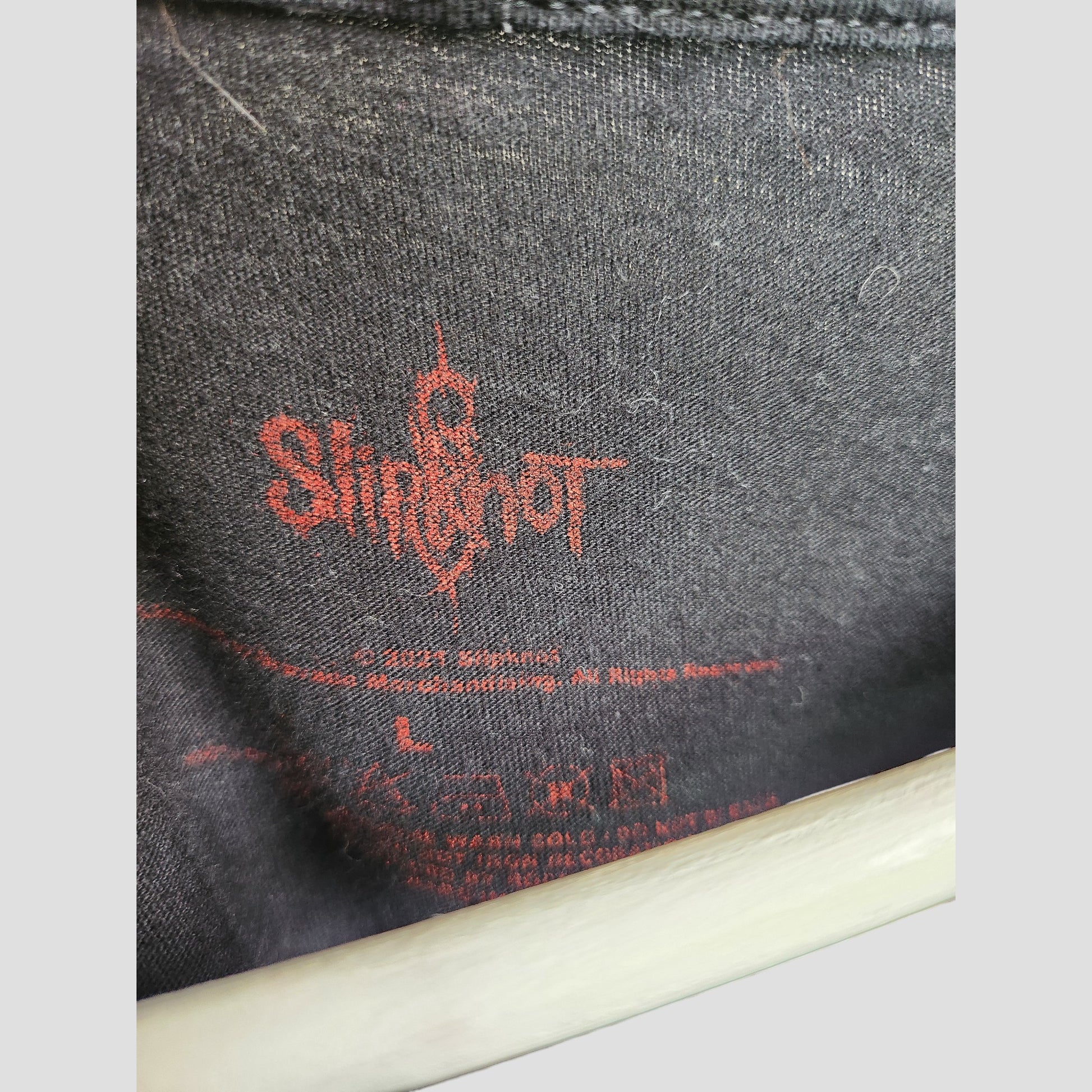 Close-up of the inside label area on an upcycled Slipknot breastfeeding & pumping t-shirt (size L), showing black fabric with red graphics, the Slipknot logo, and printed care instructions.