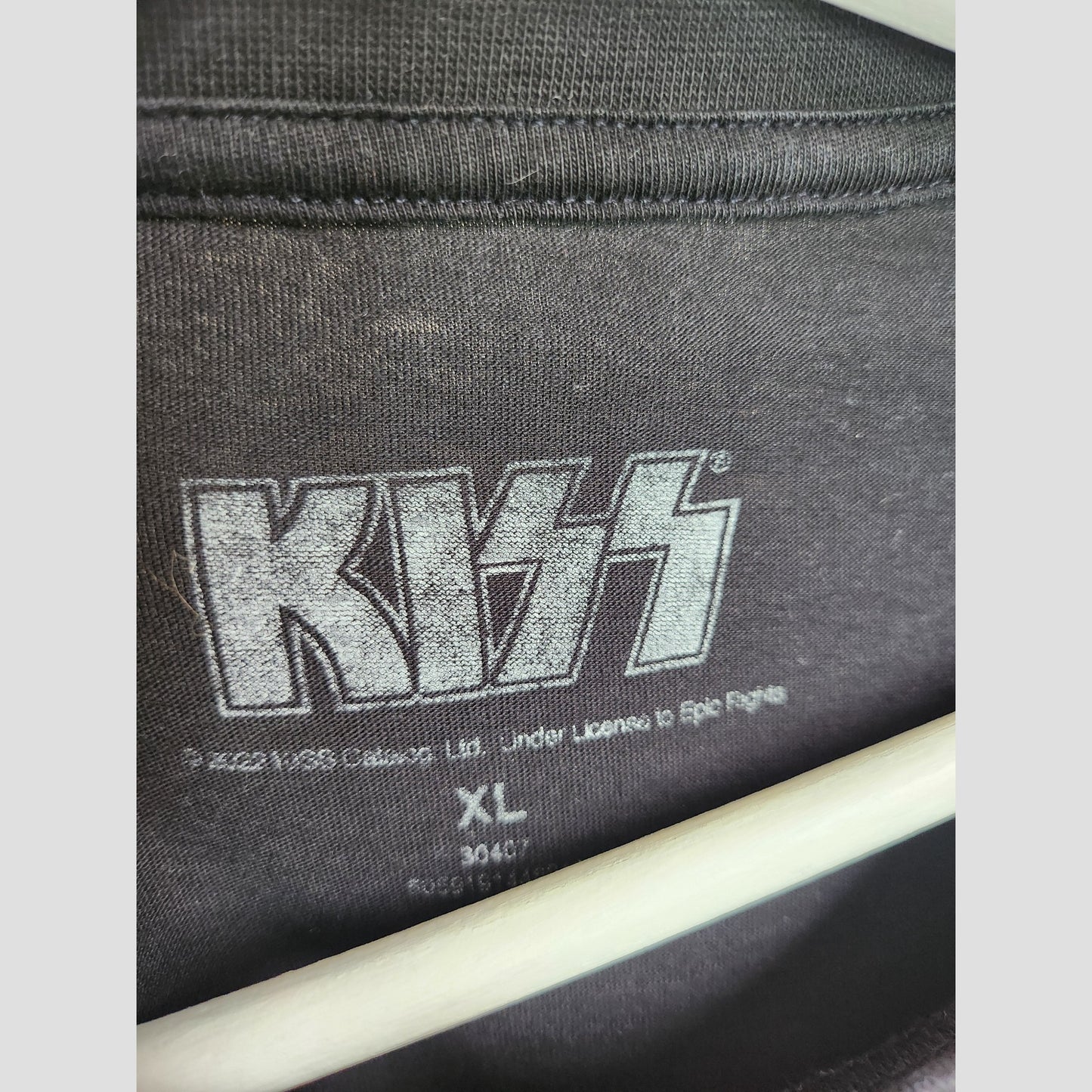 Close-up of the KISS brand Upcycled Breastfeeding & Pumping Black Faces Band T-shirt (XL, 100303) label, featuring the KISS logo in large letters and sizing info. Eco-friendly shirt is displayed on a white hanger.