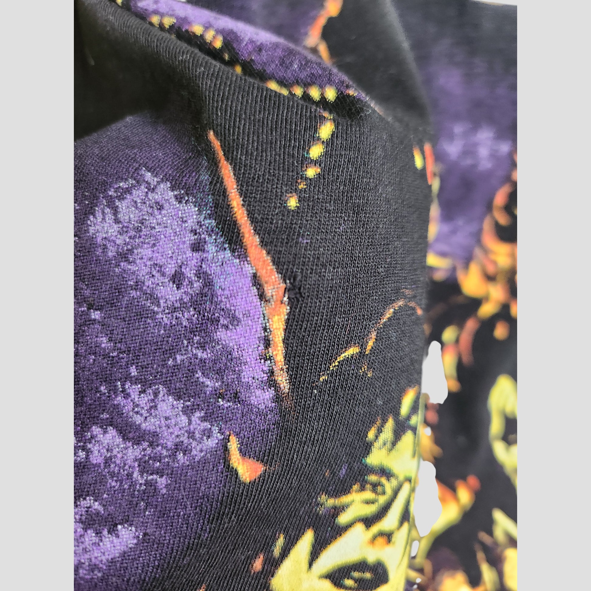 Close-up of an upcycled KISS Breastfeeding & Pumping Black Faces Band t-shirt (XL): black fabric with a vibrant, abstract yellow, orange, and purple face design and textured fiber details.