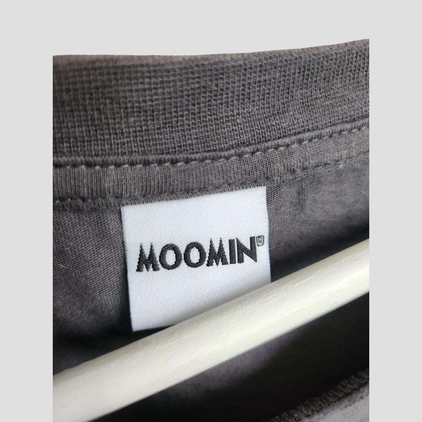 Close-up of a gray Upcycled Breastfeeding & Pumping Sunshine Moomin t-shirt (UK20) by George. Features a white tag with bold “MOOMIN” text—perfect for eco-conscious maternity wear lovers who appreciate thoughtful design.
