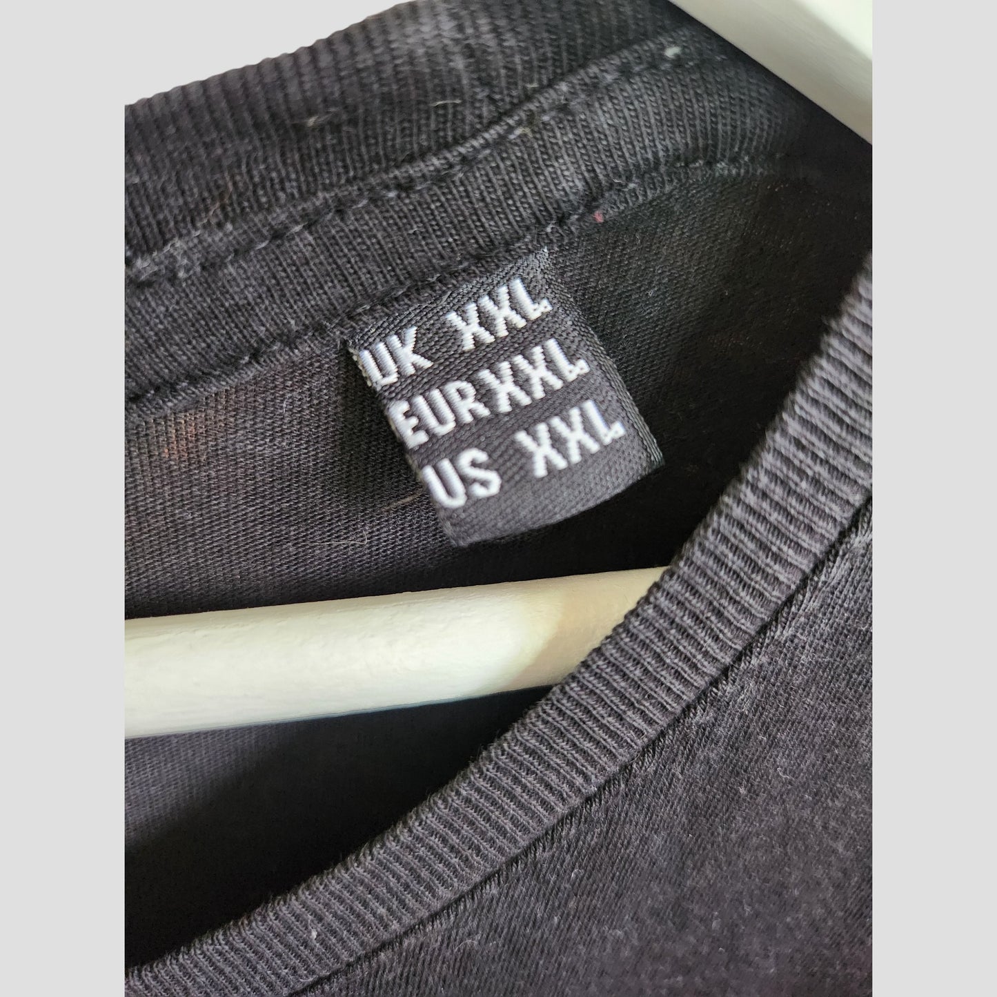 Close-up of a black Nirvana tag on an Upcycled Breastfeeding & Pumping Black/Turquoise Nirvana Band t-shirt (XXL), showing UK/EU/US XXL size, with the shirt on a white hanger.