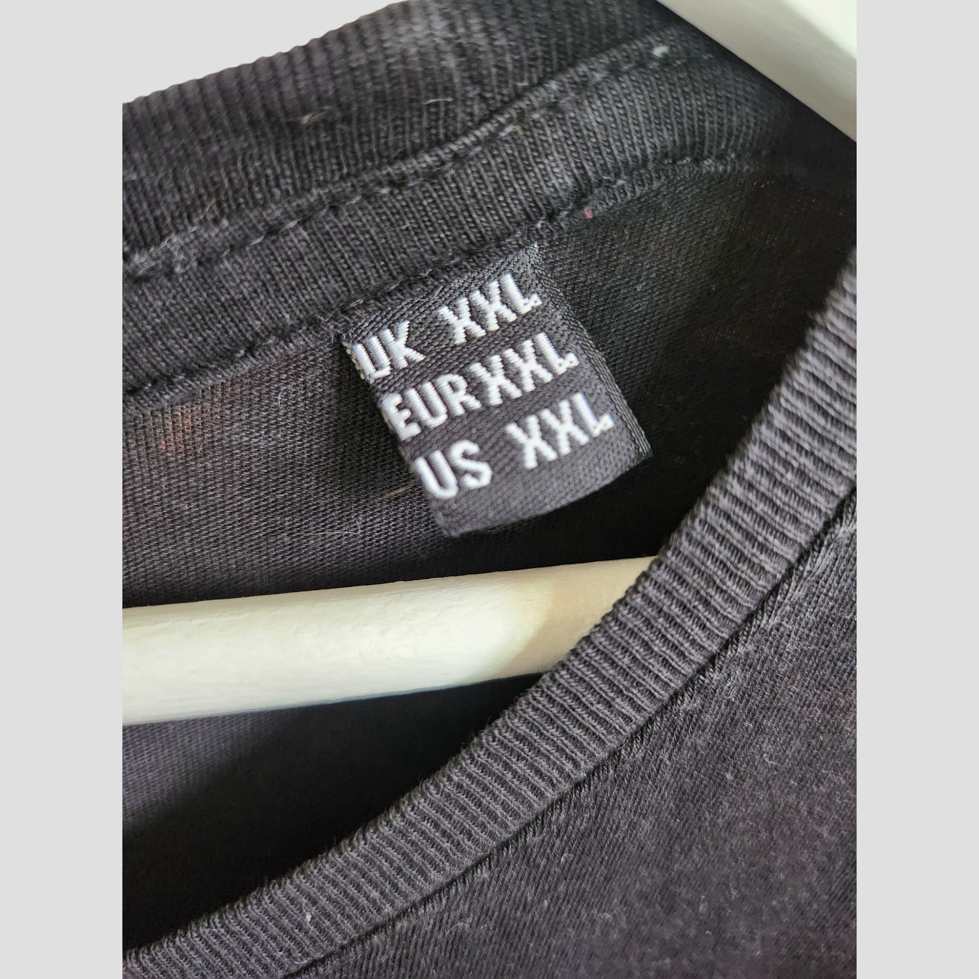 Close-up of a black Nirvana tag on an Upcycled Breastfeeding & Pumping Black/Turquoise Nirvana Band t-shirt (XXL), showing UK/EU/US XXL size, with the shirt on a white hanger.