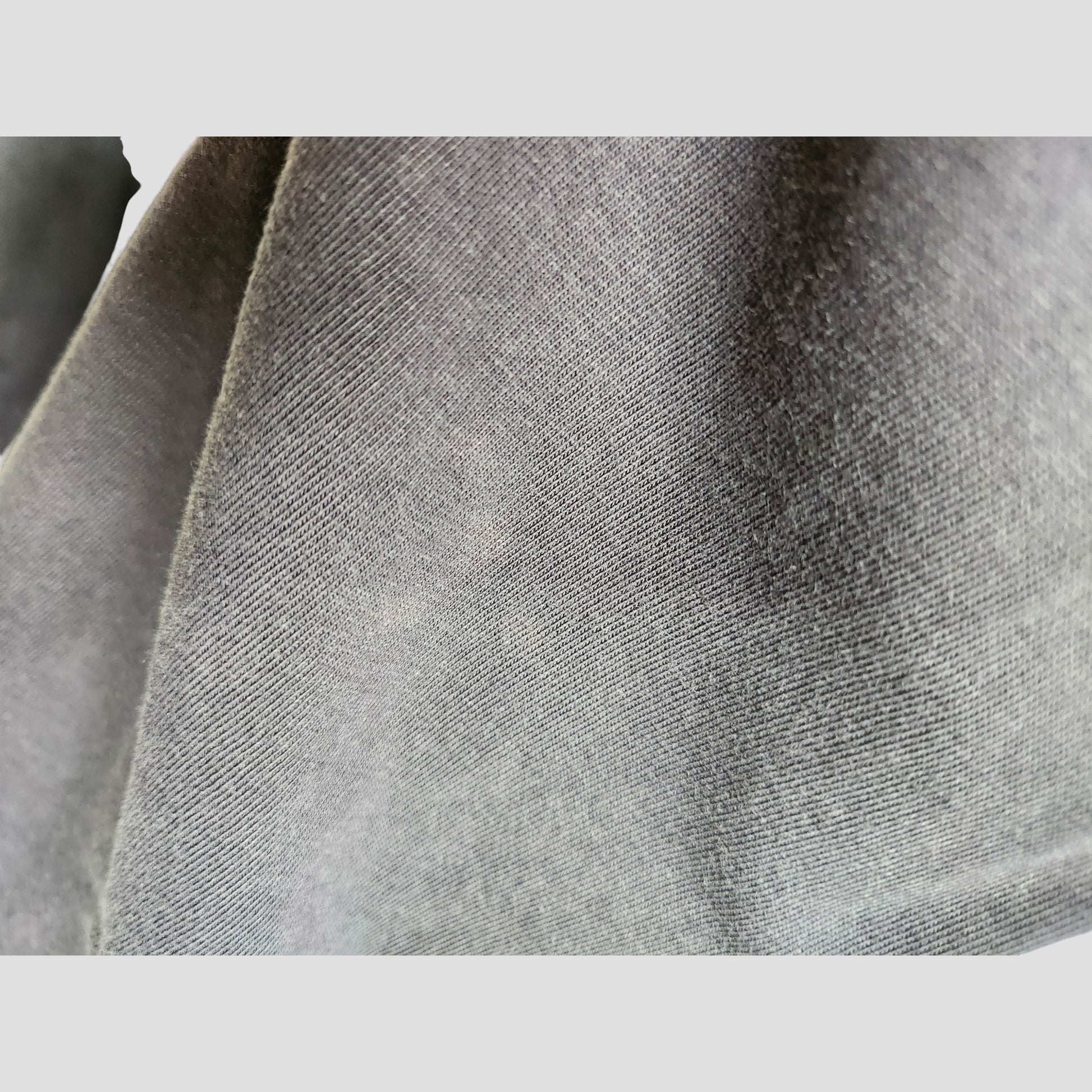 Close-up of the soft, textured grey fabric from the Primark Upcycled Breastfeeding (Nursing) & Pumping The Rolling Stones US Tour Band t-shirt XL (UK18/20), showing fine threads, subtle wrinkles, and a diagonal pattern—perfect for eco-friendly nursing wear.