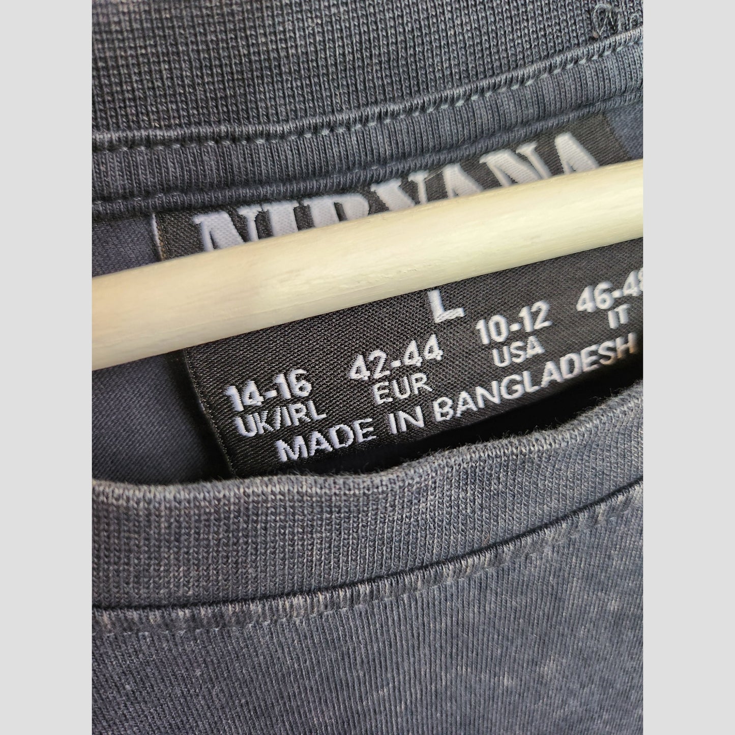 Close-up of a Primark Upcycled Breastfeeding & Pumping Grey/Turquoise Angel Nirvana Band T-shirt (L UK14/16, 100293) label on hanger, showing size info for UK/EUR/USA/Italy. Made in Bangladesh—ideal for eco-friendly nursing fashion fans.