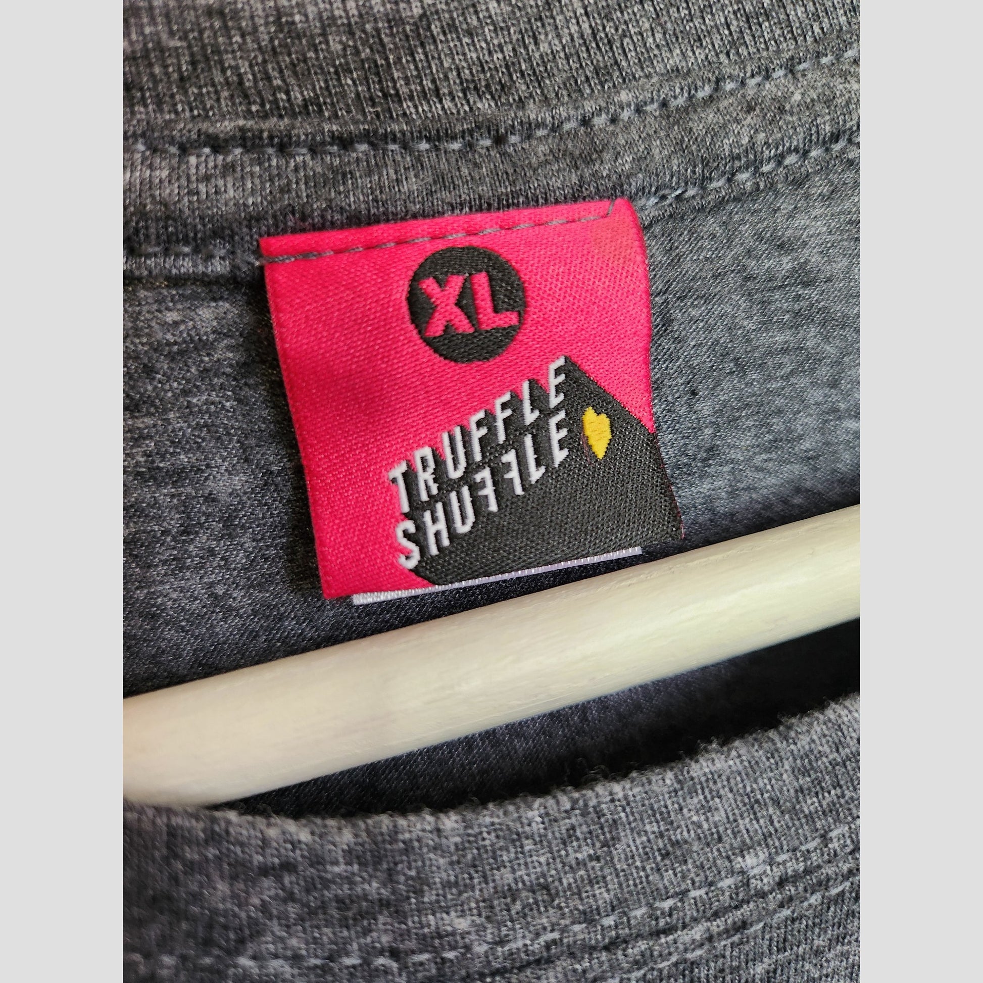 A close-up of the collar on a gray XL Truffle Shuffle Upcycled Breastfeeding & Pumping Washed Out Toroto t-shirt, featuring a pink and black label with white text and a yellow heart—ideal for eco-conscious fans of preloved clothing.