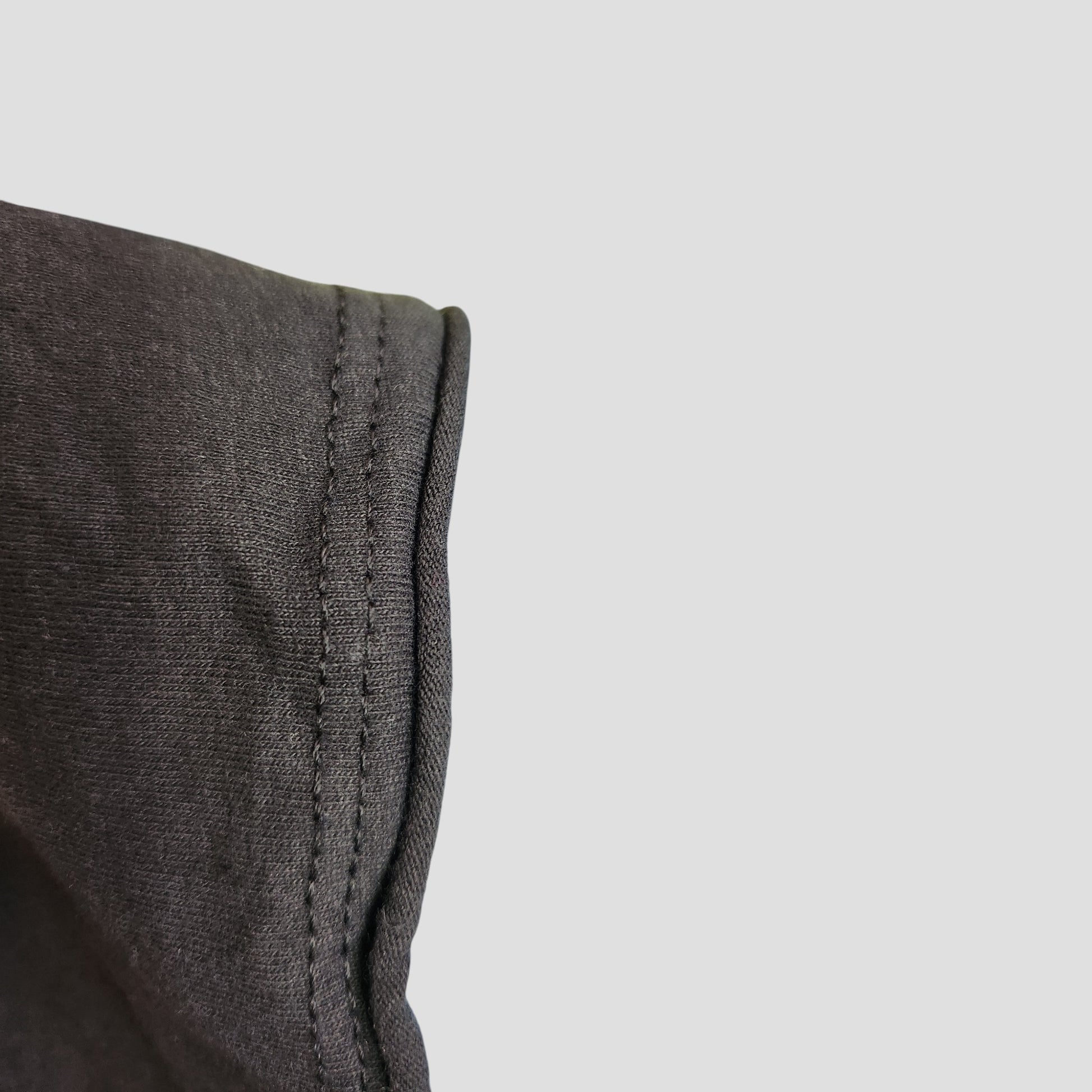 Close-up of visible stitching on a dark grey Upcycled Breastfeeding & Pumping AC/DC Band t-shirt (XL) by Amplified, set against a light gray background—perfect for highlighting eco-friendly maternity fashion details.