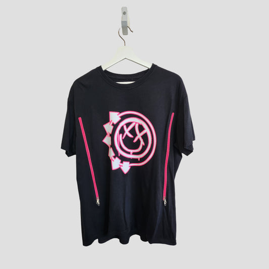 The Blink 182 Upcycled Breastfeeding & Pumping Black/Pink Band T-shirt XL (100341) features a large pink and white smiley logo and two vertical pink zippers on each side, shown on a white hanger against a light gray background.