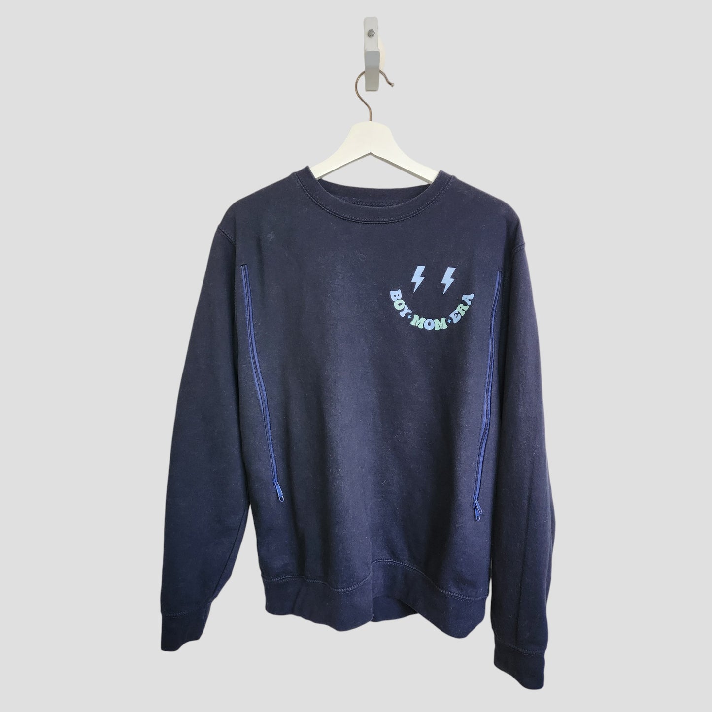 The My Rocking Kids Upcycled Breastfeeding & Pumping Boy Mom Era Sweatshirt (M, 100142) is navy blue with two lightning bolts and "BOY MOM ERA" in light blue on the chest, shown on a white hanger against a plain light background.
