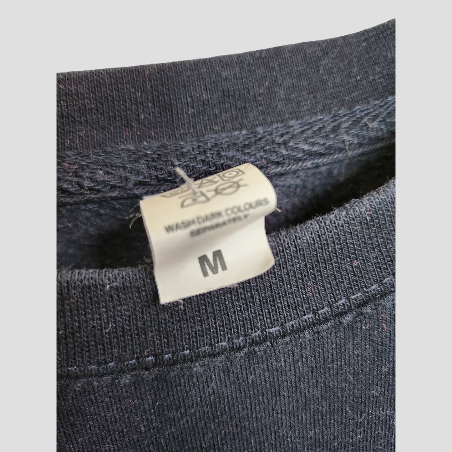 Close-up of the inside collar of the My Rocking Kids Upcycled Breastfeeding & Pumping Boy Mom Era Sweatshirt (M, 100142), showing a white size tag and wash instructions to wash dark colors separately. Made from eco-friendly maternity fabric.