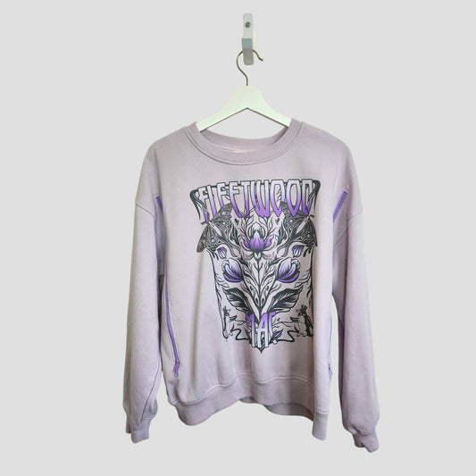 A lilac H&M upcycled breastfeeding & pumping Fleetwood Mac band sweatshirt (L, 100135) hangs on a white hanger, showcasing bold black and purple graphics with floral and geometric designs—eco-friendly, stylish, and affordable.