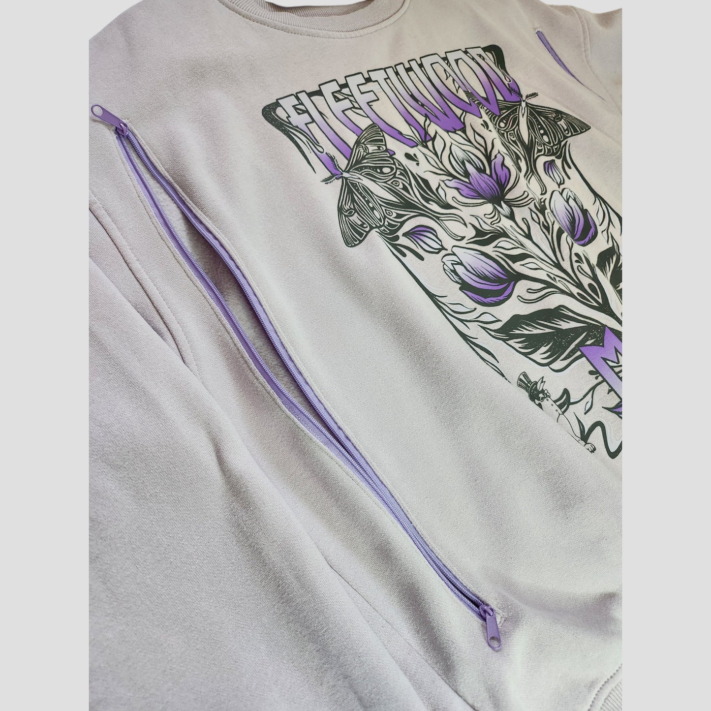 The H&M Upcycled Breastfeeding & Pumping Lilac Fleetwood Mac Band Sweatshirt (L, 100135) features lavender diagonal zippers, a floral and butterfly graphic with "Fleetwood" text, and is crafted from eco-friendly materials.