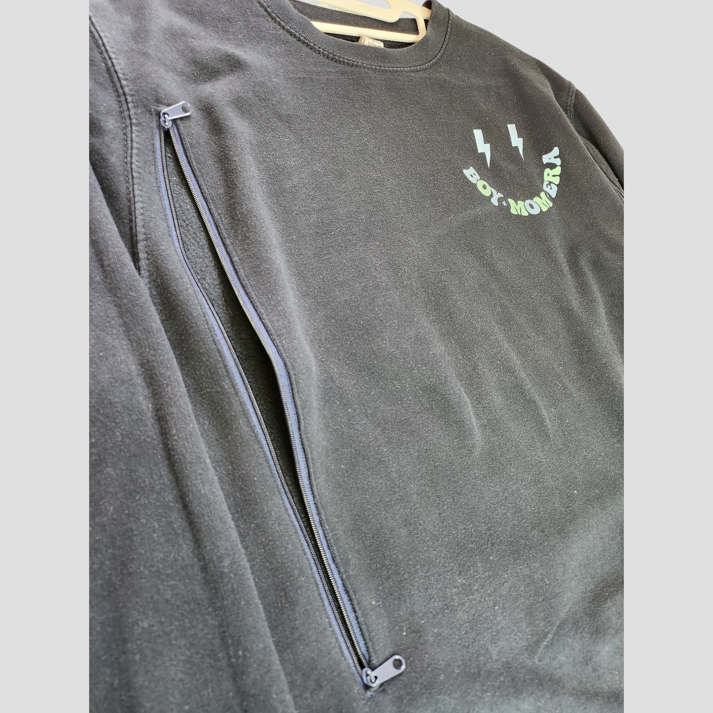 The Upcycled Breastfeeding & Pumping Boy Mom Era Sweatshirt by My Rocking Kids showcases a black design with a diagonal front zipper and “BOT MOVERS” lightning graphic—ideal eco-friendly nursing wear.