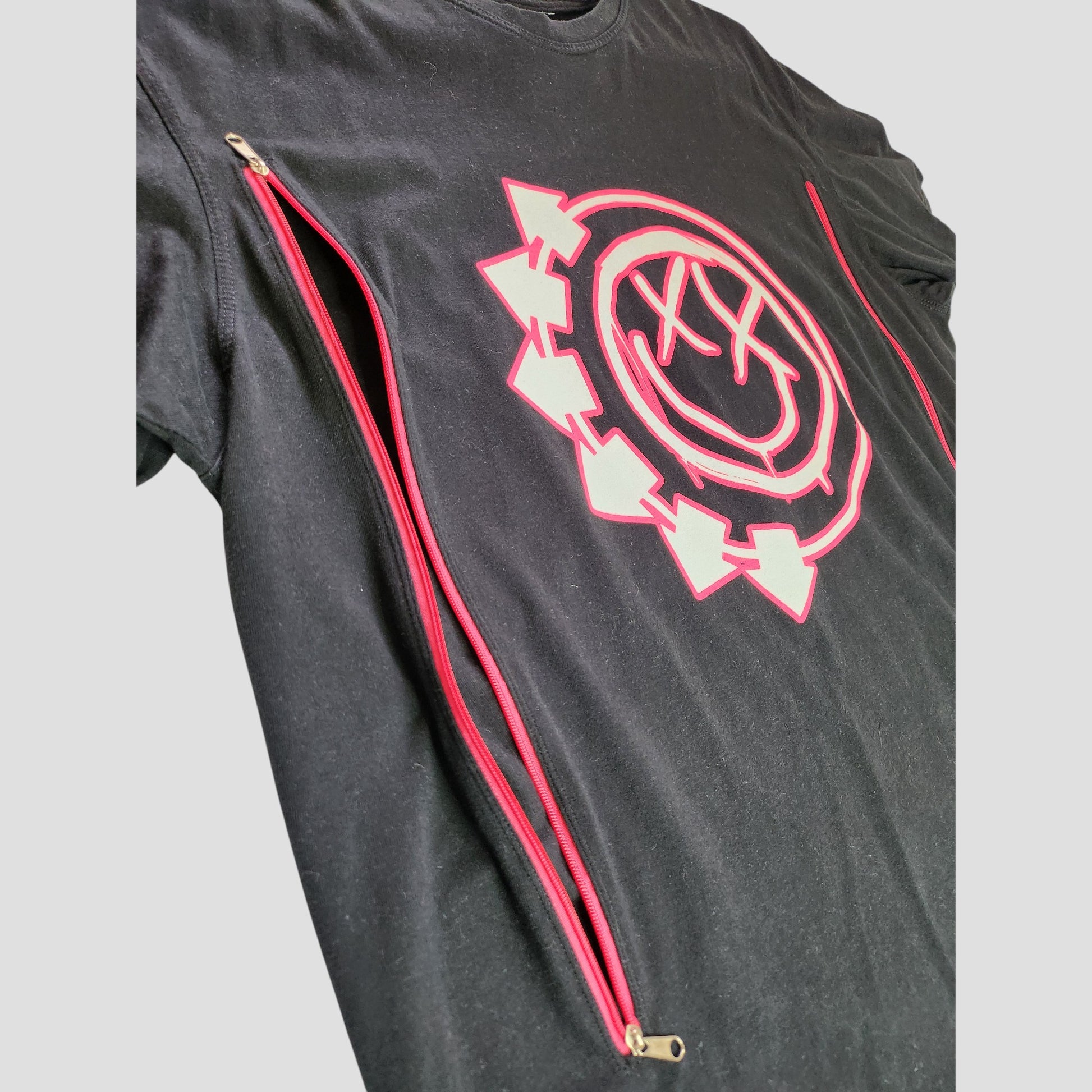 The Blink 182 Upcycled Breastfeeding & Pumping Black/Pink Band t-shirt (XL, 100341) features red side zippers and a neon pink smiley face with X eyes and arrows on the chest, made from preloved clothing.