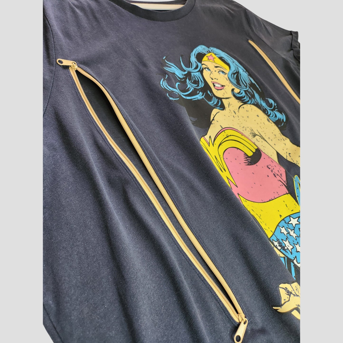 A close-up of Tu’s Upcycled Breastfeeding & Pumping Navy Wonder Women t-shirt UK24, featuring a vibrant Wonder Woman graphic and diagonal zippers—ideal eco-friendly maternity wear.