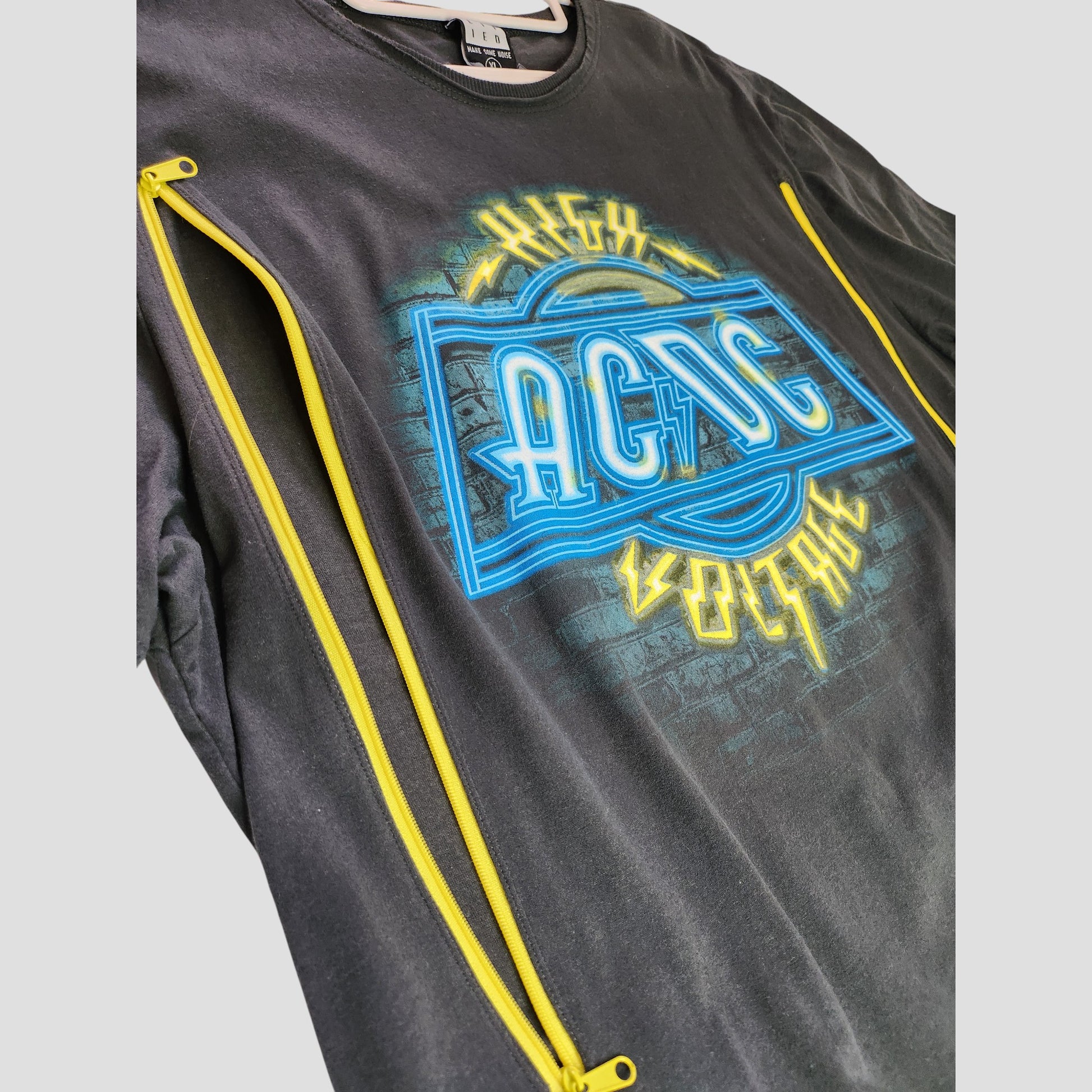 Upcycled Amplified grey AC/DC band t-shirt (XL), crafted from breastfeeding clothing, features a neon blue and yellow High Voltage graphic and two diagonal yellow side zippers for an edgy, sustainable look.