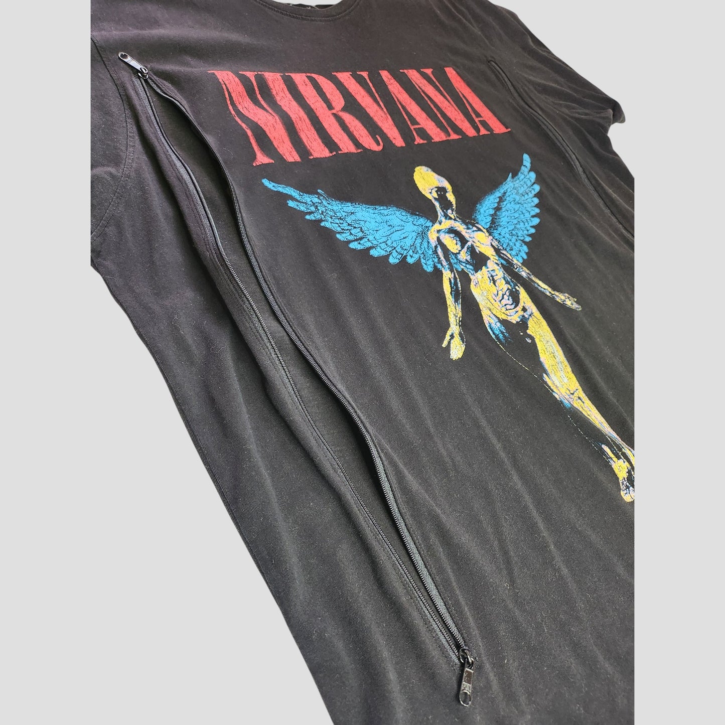Nirvana Upcycled Breastfeeding & Pumping Black/Turquoise Band T-shirt (XXL, 100302): Features "NIRVANA" in red above a blue/yellow winged figure and a diagonal black zipper for nursing or pumping. Crafted from upcycled clothing.