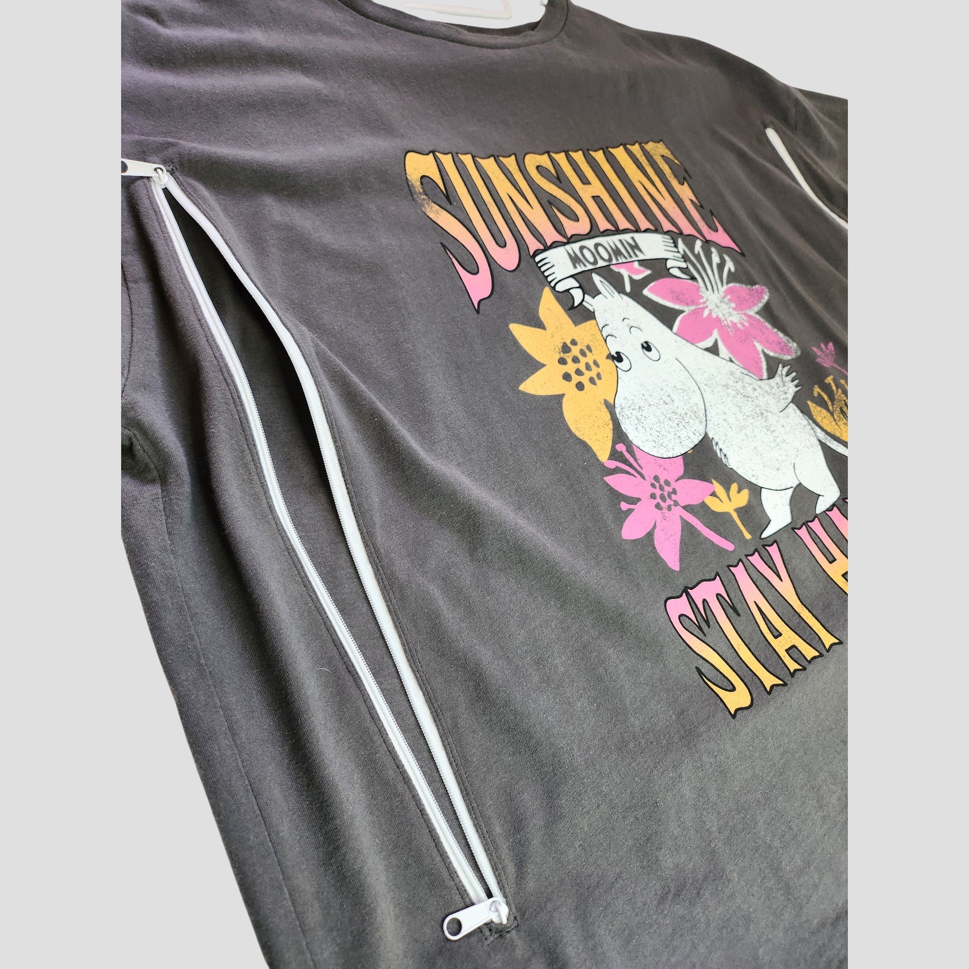 The George Upcycled Breastfeeding & Pumping Sunshine Moomin t-shirt UK20 is a dark gray eco-friendly maternity top with a Moomin, yellow and pink flowers, "SUNSHINE STAY HAPPY" text, and two diagonal white zippers for nursing.