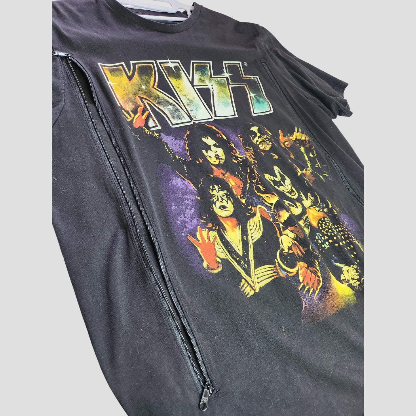 This upcycled XL black KISS Faces Band T-shirt features a colorful graphic, diagonal left-side zipper, and is crafted from breastfeeding clothing for a unique, sustainable style. Brand: KISS. Product: Upcycled Breastfeeding & Pumping T-shirt (100303).