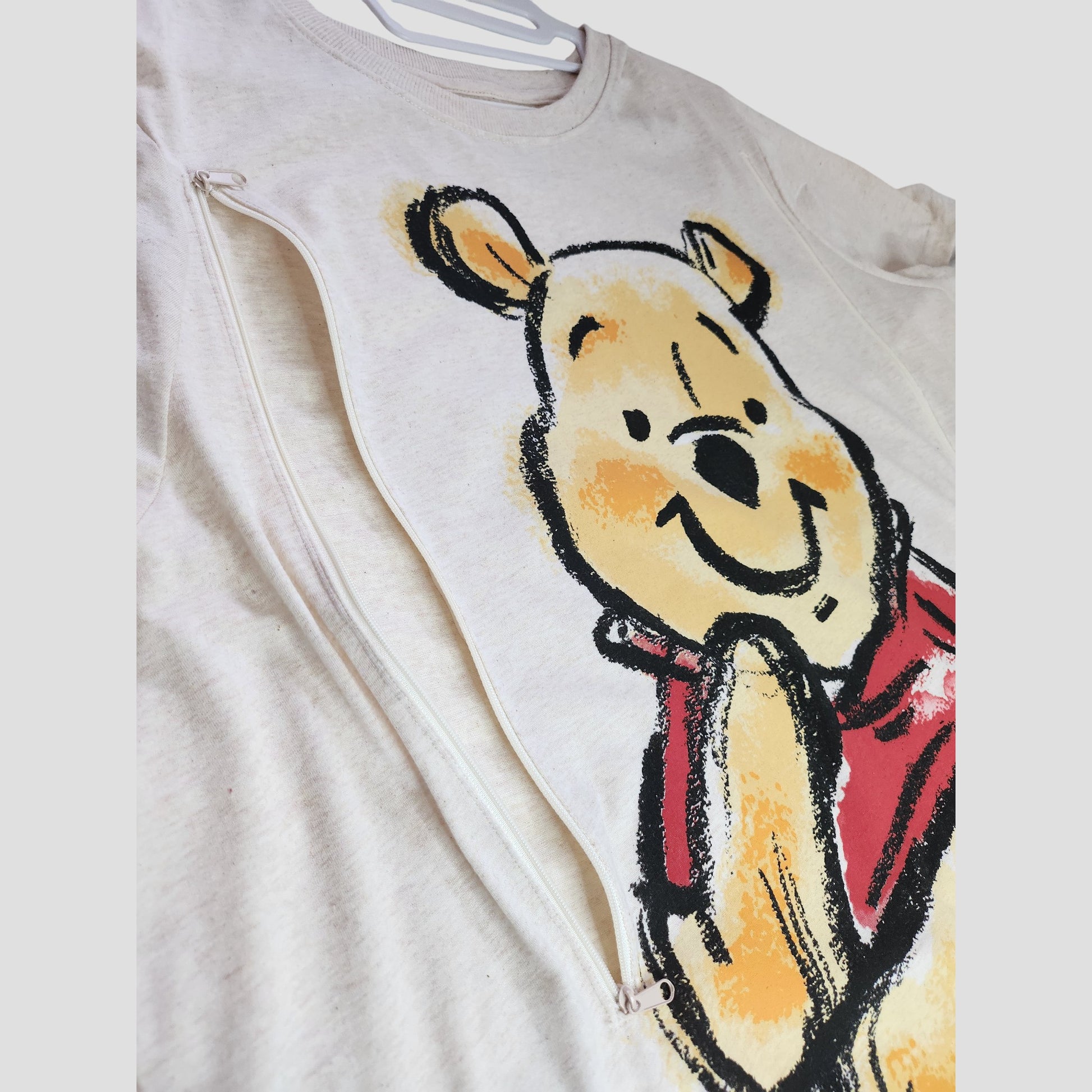 The Primark Upcycled Cream Winnie the Pooh Nursing & Pumping t-shirt (2XL, UK22/24) features a smiling Pooh design and side zipper for breastfeeding—ideal eco-friendly maternity wear for Disney fans.