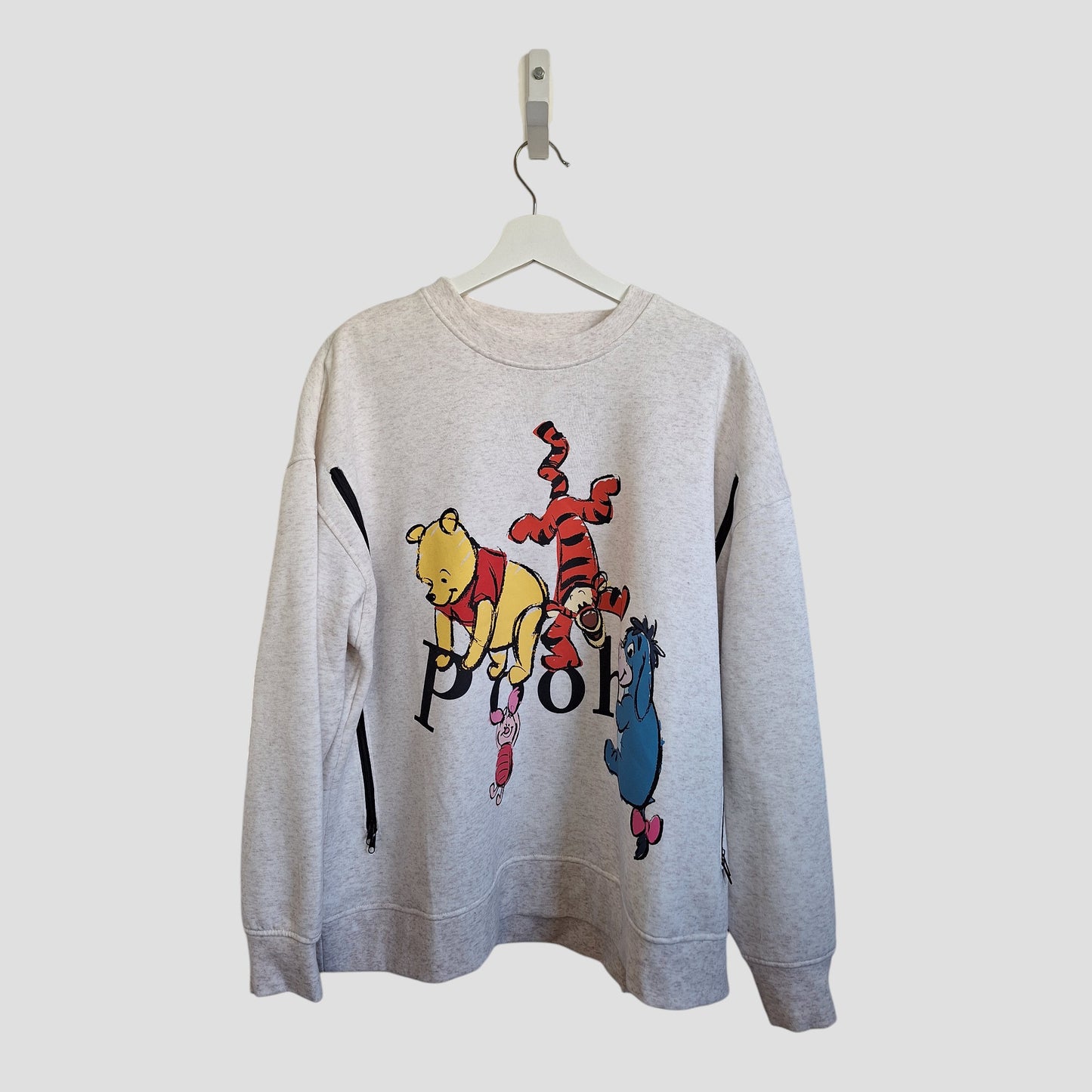 A Primark Upcycled Breastfeeding & Pumping Cream Winnie the Pooh Sweatshirt (XL, UK18/20) hangs on a hanger, with illustrations of Winnie the Pooh, Tigger, and Eeyore above partially visible "POOH" text on the front.