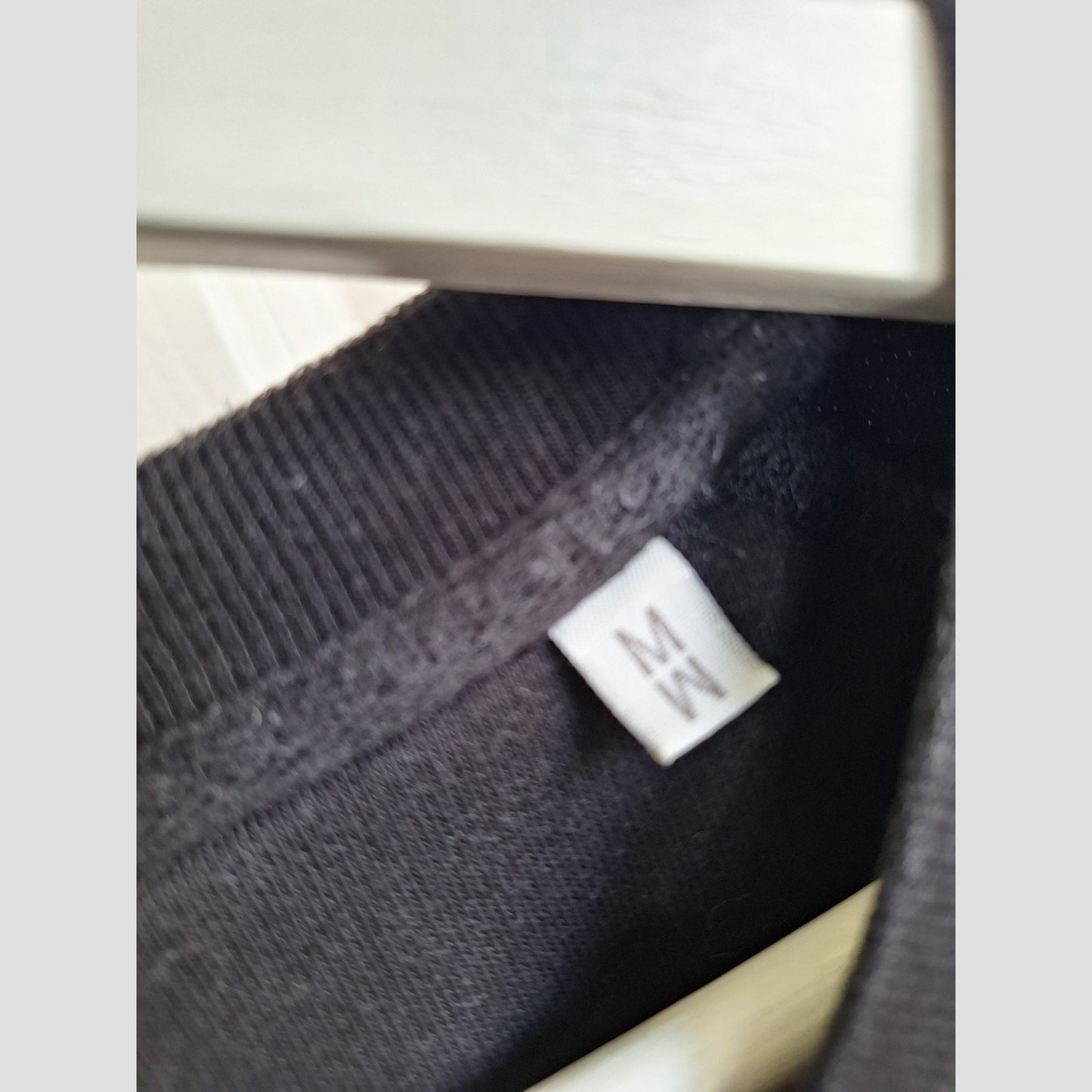 A close-up of the Selfish Mother Upcycled Breastfeeding & Pumping Black/Gold MOTHER Sweatshirt’s neckline on a hanger, featuring a white “MW” tag—ideal for those seeking eco-friendly maternity wear.