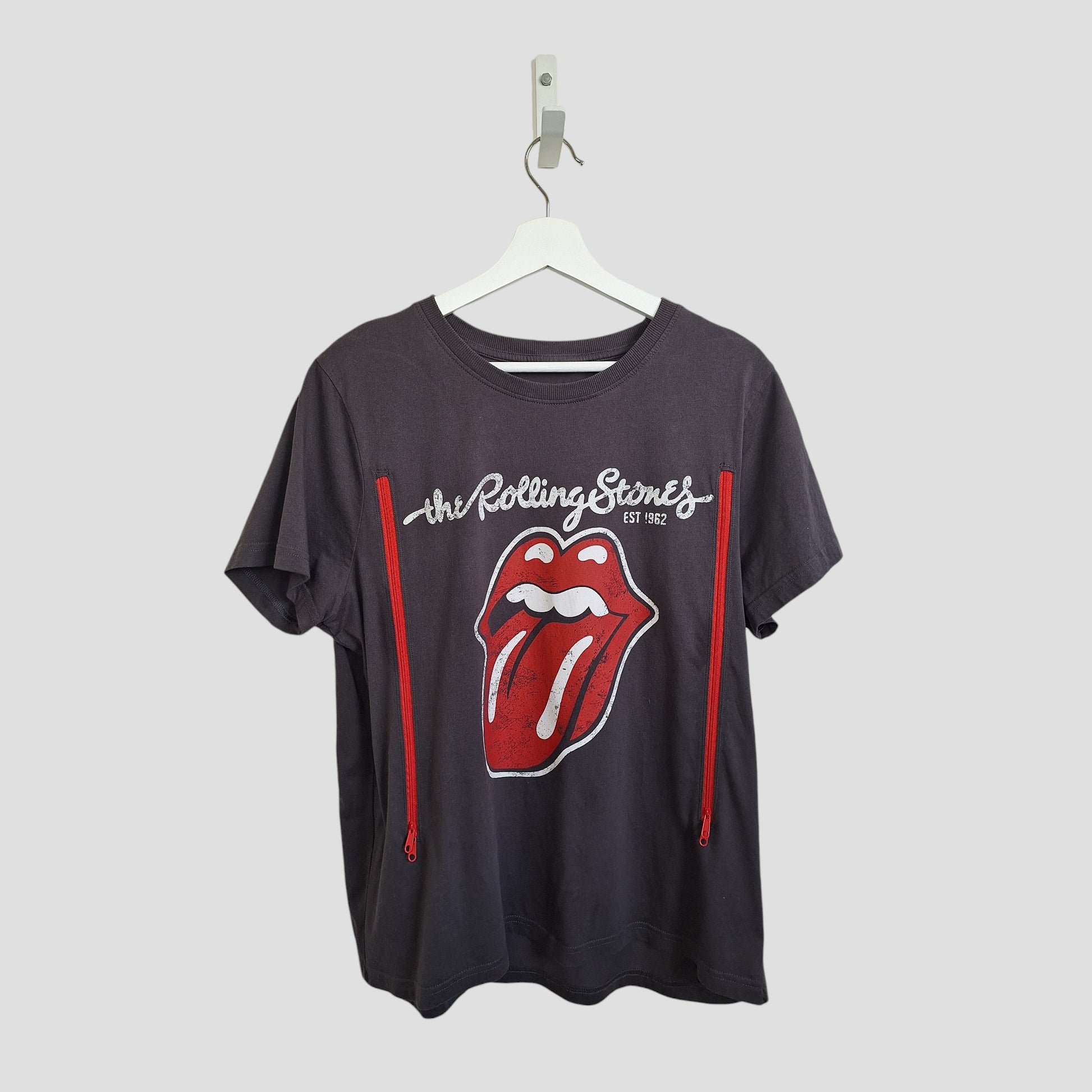 A grey upcycled Primark Rolling Stones nursing & pumping band t-shirt (L), featuring the band's name and logo, made from preloved clothing, hangs on a white hanger against a plain light background.