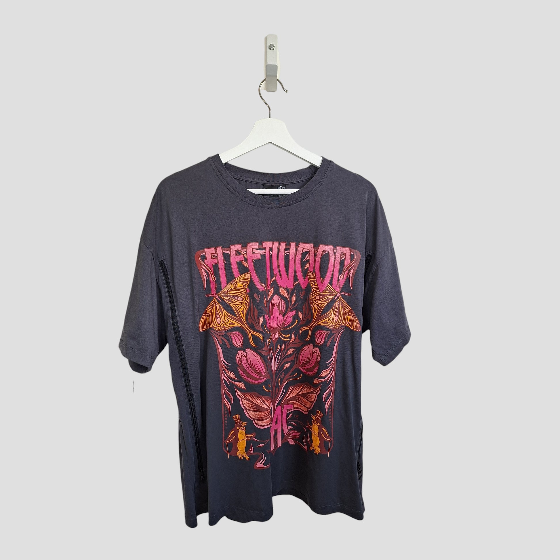 A dark upcycled Primark t-shirt (UK12/14), designed for breastfeeding & pumping, hangs on a white hanger with a vibrant floral, butterfly graphic and bold pink “FLEETWOOD” text across the chest. Fleetwood Mac band style.