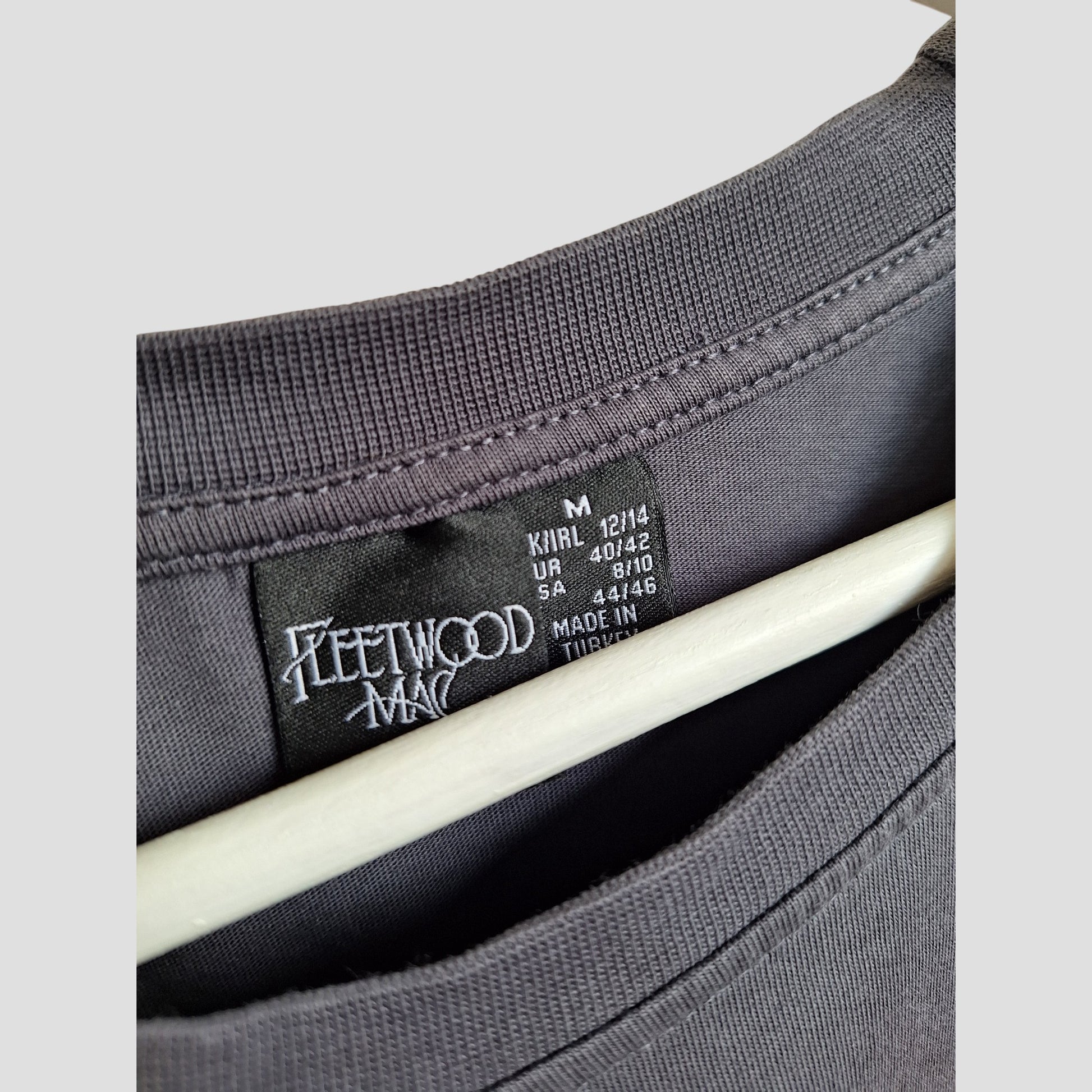 Close-up of a Primark Upcycled Breastfeeding & Pumping Floral Fleetwood Mac Band t-shirt (M/UK12/14), showcasing the logo label, size info, and Made in Turkey—an eco-friendly, stylish pick for music-loving moms.