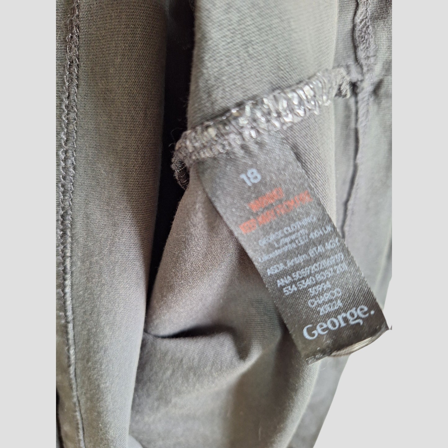 A close-up of a black fabric tag inside this upcycled George maternity nursing/pumping Iron Maiden band t-shirt (UK18), featuring care instructions in white and red. Part of our preloved maternity clothes selection.