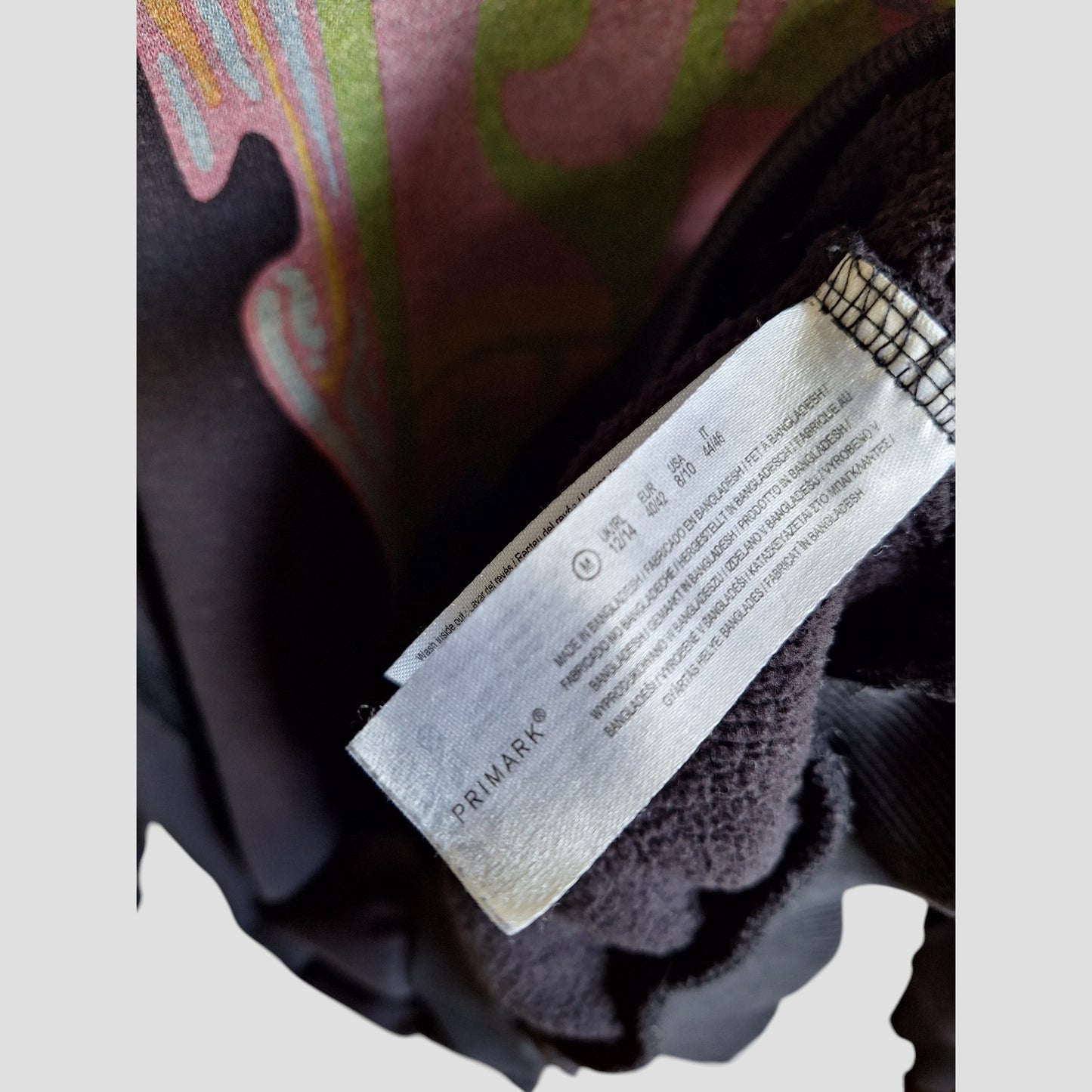 A close-up of a Primark fabric label with washing instructions inside an upcycled breastfeeding & pumping Pink Floyd sweatshirt (M/UK12-14), perfect for those seeking preloved maternity wear.