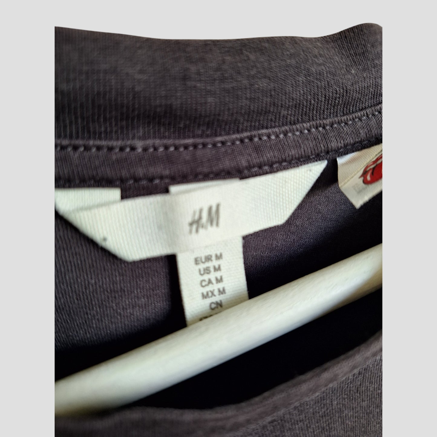 Close-up of an H&M Upcycled Breastfeeding & Pumping Rainbow The Rolling Stones Band t-shirt (M, 100193) on a hanger, showing multi-country size tags and visible eco-friendly fabric—perfect for maternity fashion needs.