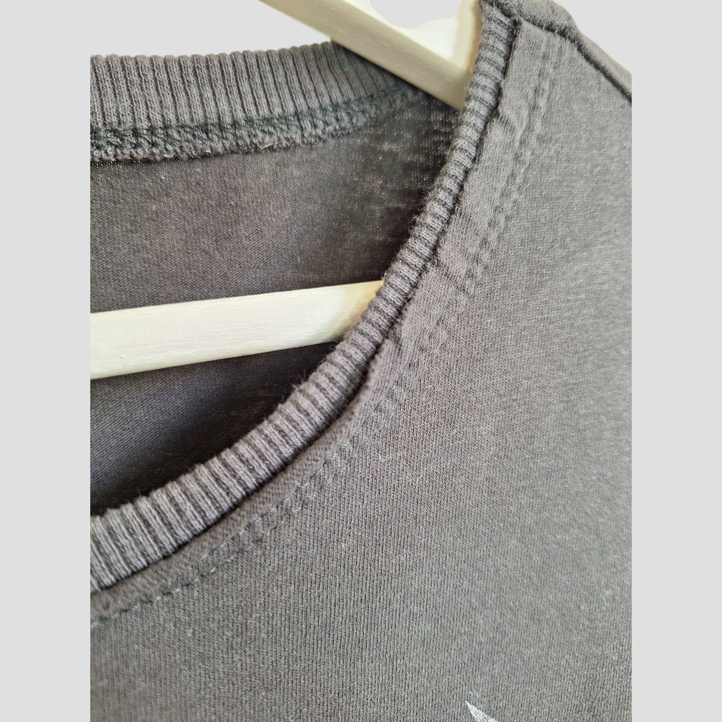 Close-up of the neckline and shoulder seam of an Amplified Upcycled Breastfeeding & Pumping Metallica Guitar Band t-shirt XL (100353) on a light wooden hanger, highlighting fabric texture and stitching—crafted from preloved clothing.