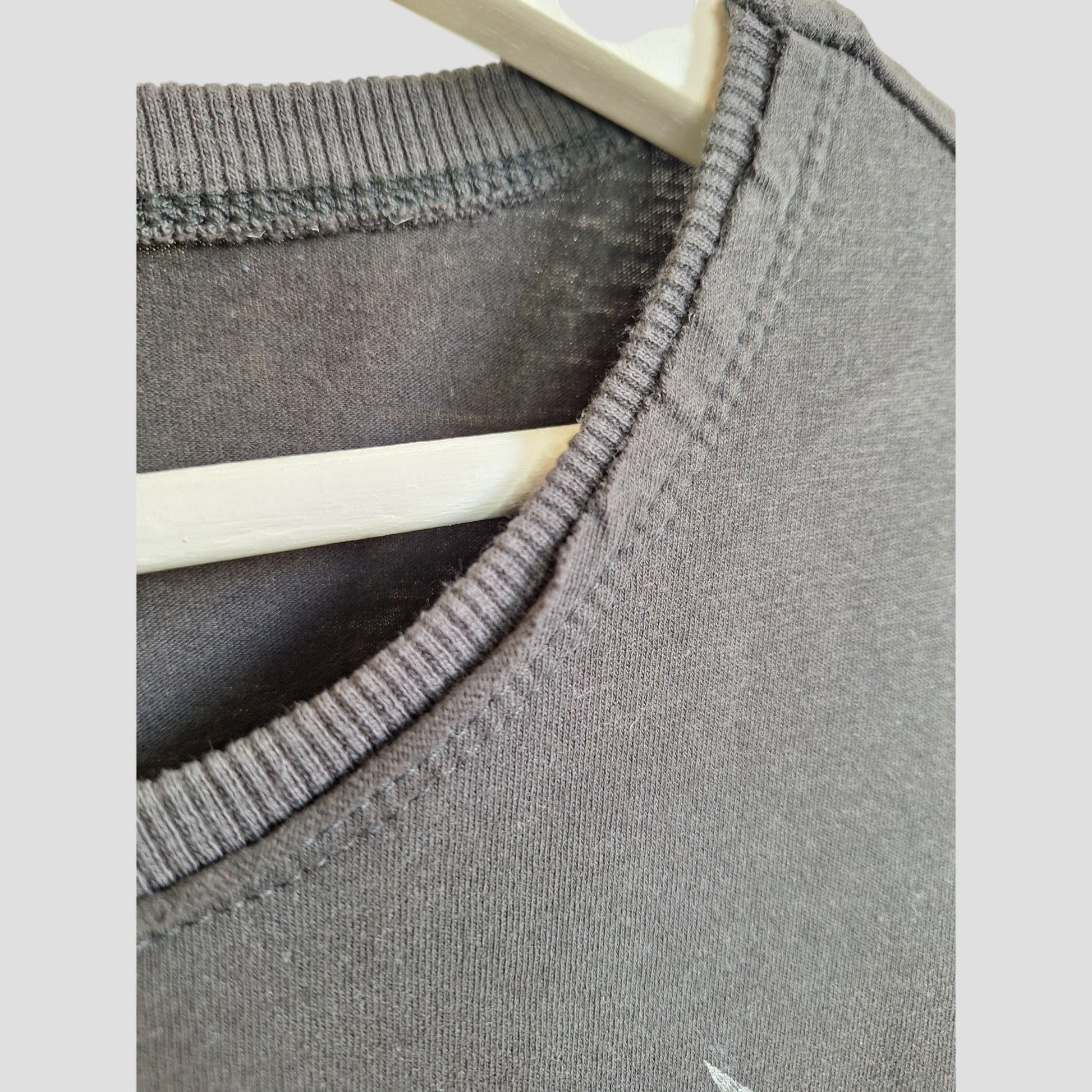 Close-up of the neckline and shoulder seam of an Amplified Upcycled Breastfeeding & Pumping Metallica Guitar Band t-shirt XL (100353) on a light wooden hanger, highlighting fabric texture and stitching—crafted from preloved clothing.