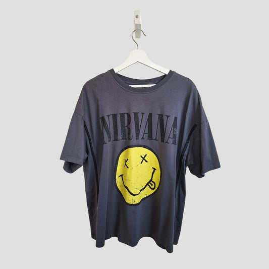 A dark gray Primark Upcycled Breastfeeding & Pumping Nirvana Band t-shirt (L, UK14/16) hangs on a white hanger, featuring large black “Nirvana” lettering above a yellow smiley face logo with crossed-out eyes.