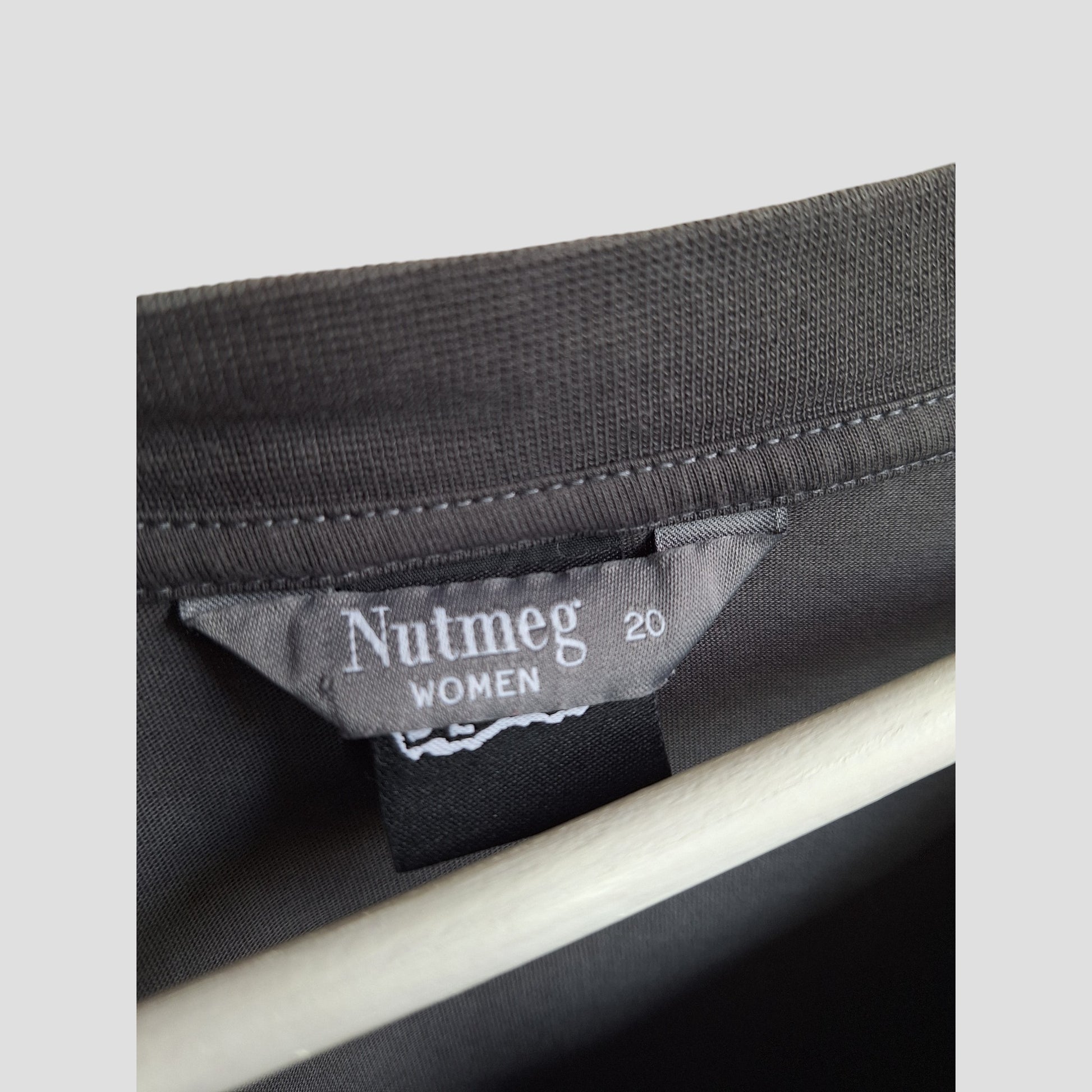 Close-up of a gray Nutmeg label inside a UK20 upcycled breastfeeding and pumping Grey Blondie Band t-shirt, stitched onto dark fabric—perfect for those seeking eco-friendly maternity wear.